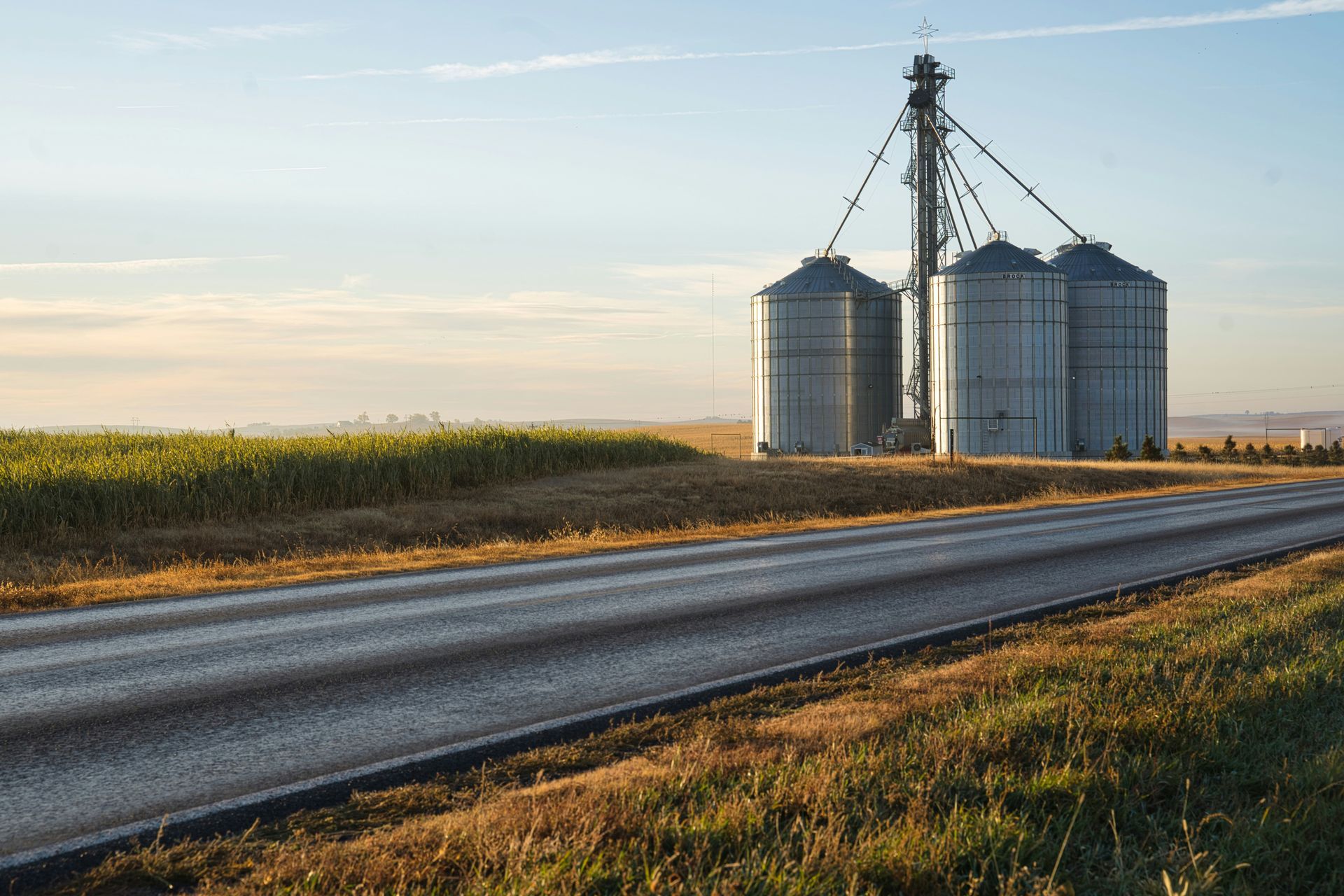 Grain silos beside a road in a field, under a blue sky.