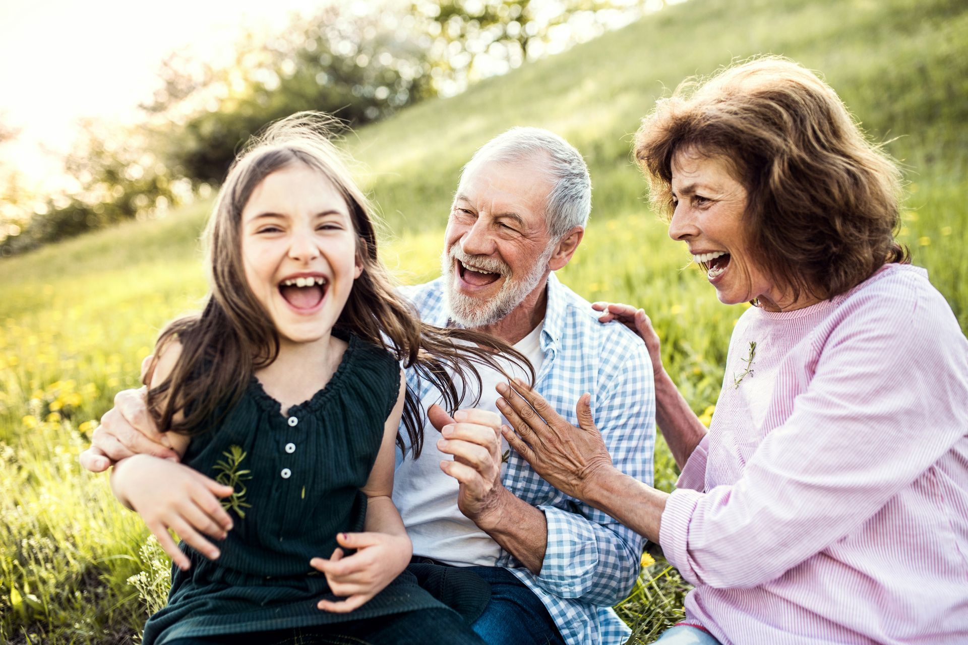 Girl laughing with grandparents in a grassy field. Sunshine.