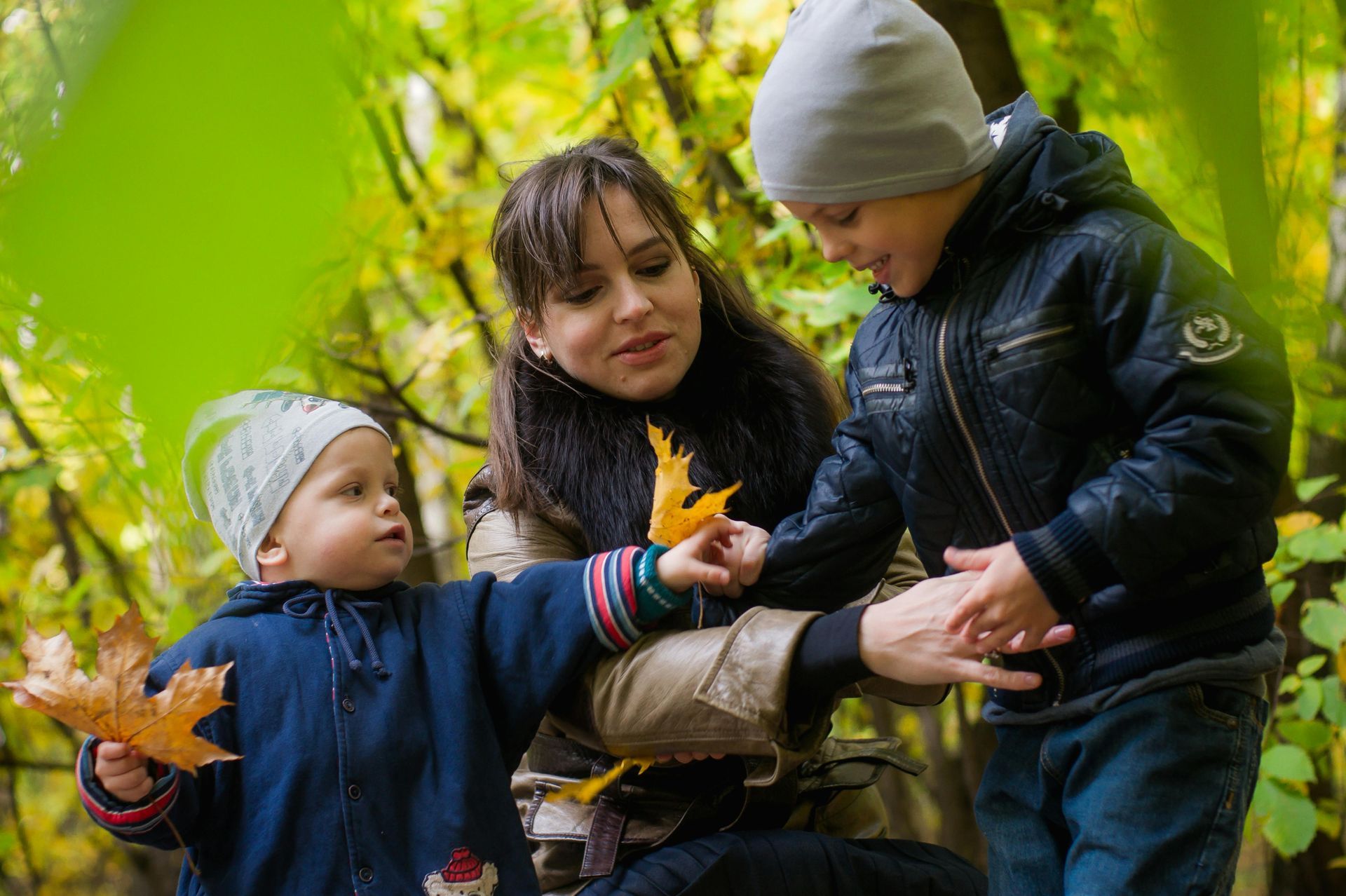 Woman and two children in a forest, looking at fallen leaves.