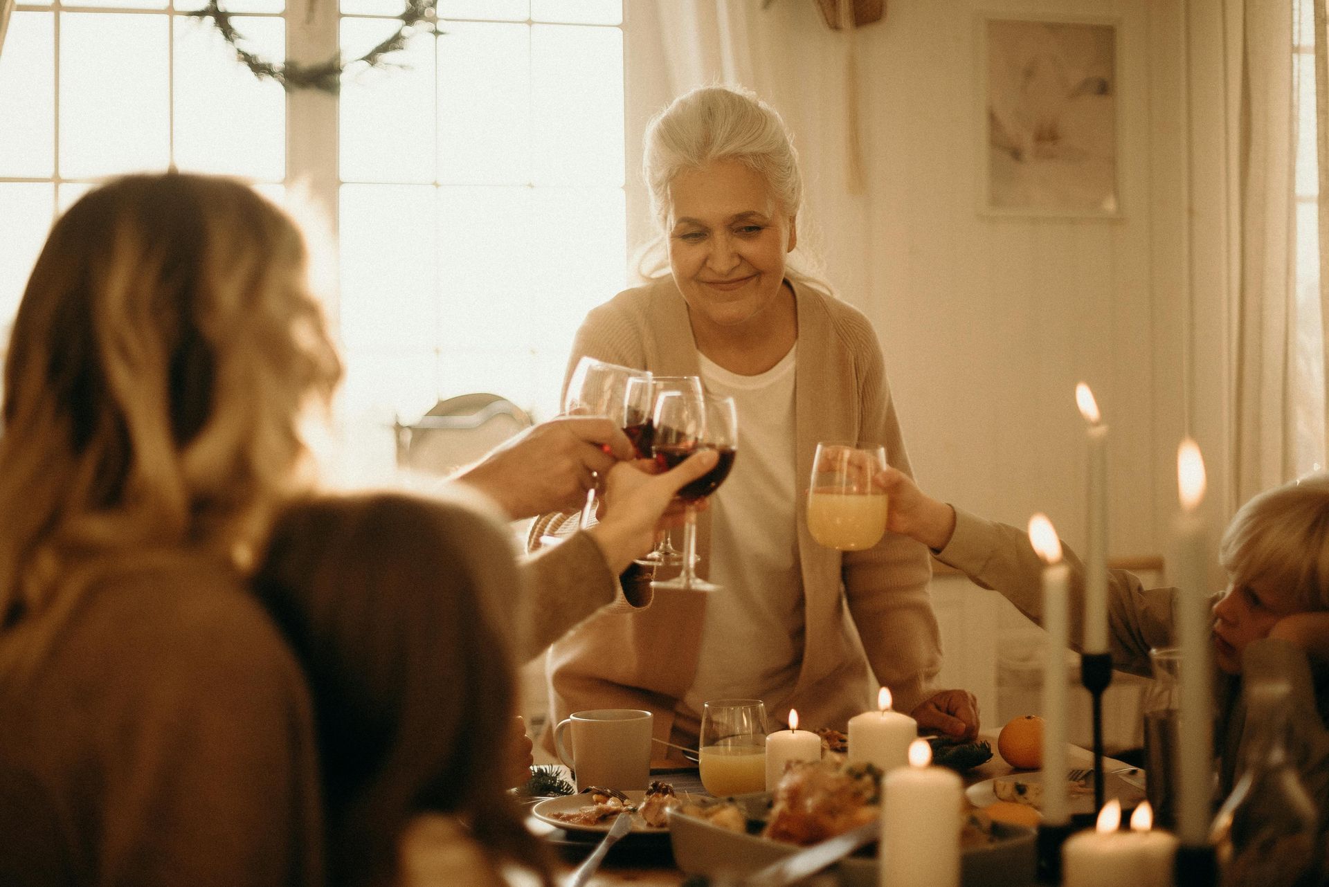 Family cheers with drinks around a candlelit dinner table. Grandmother smiles, offering a toast.