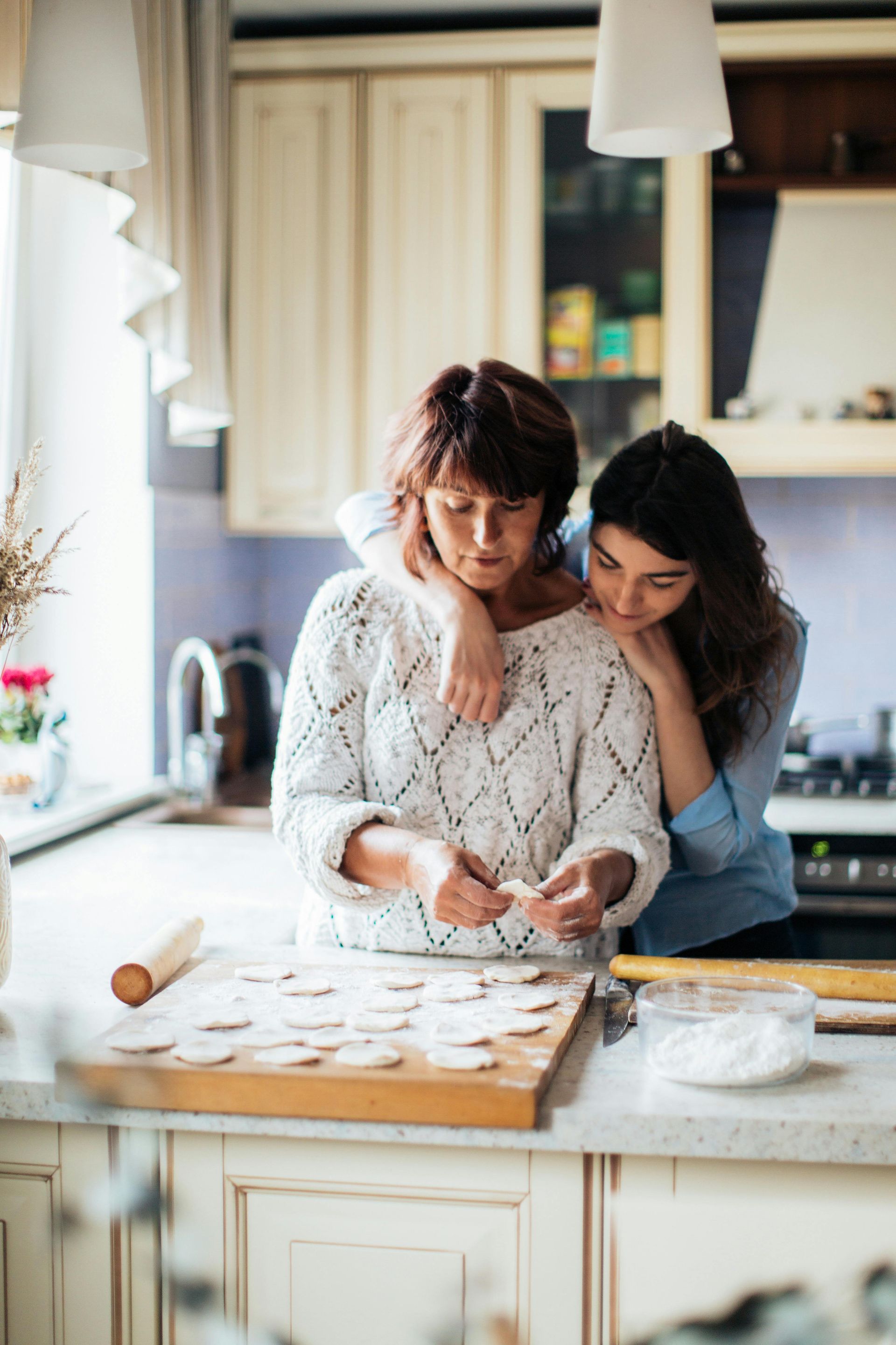 Woman making cookies in kitchen, embraced by another woman.