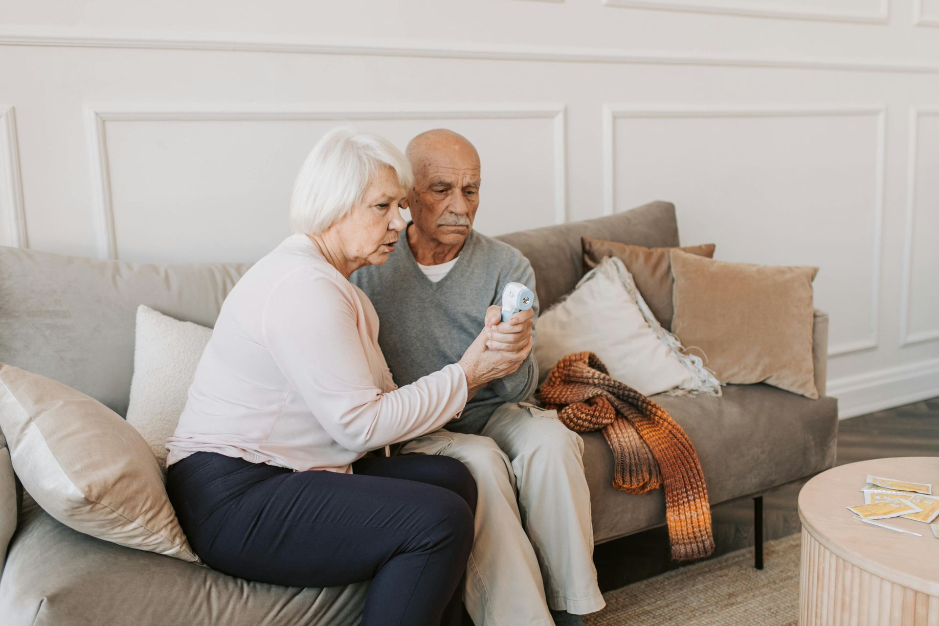 An older couple on a sofa, looking at a prescription bottle; living room setting.