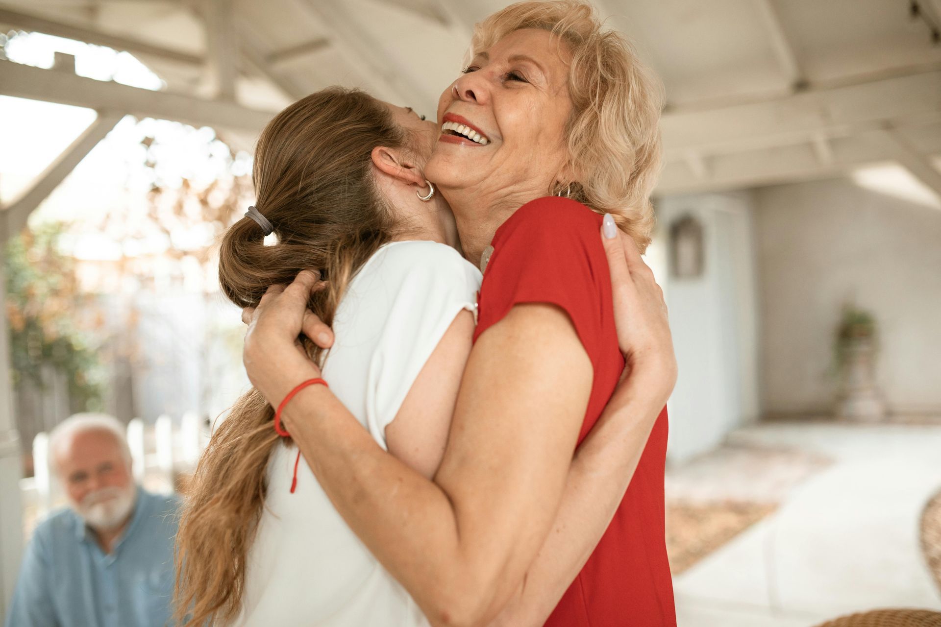 Woman hugs older woman; both smiling, outdoors.