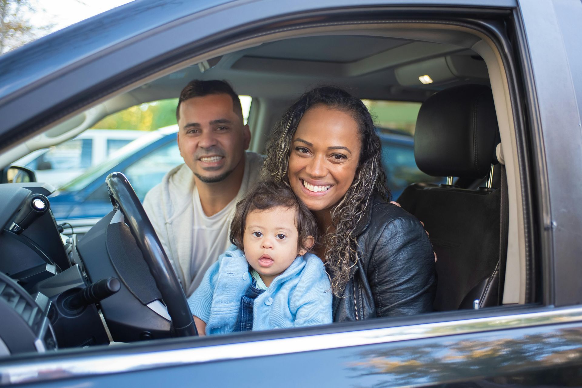 Family smiling in a car; parents, infant with Down syndrome.