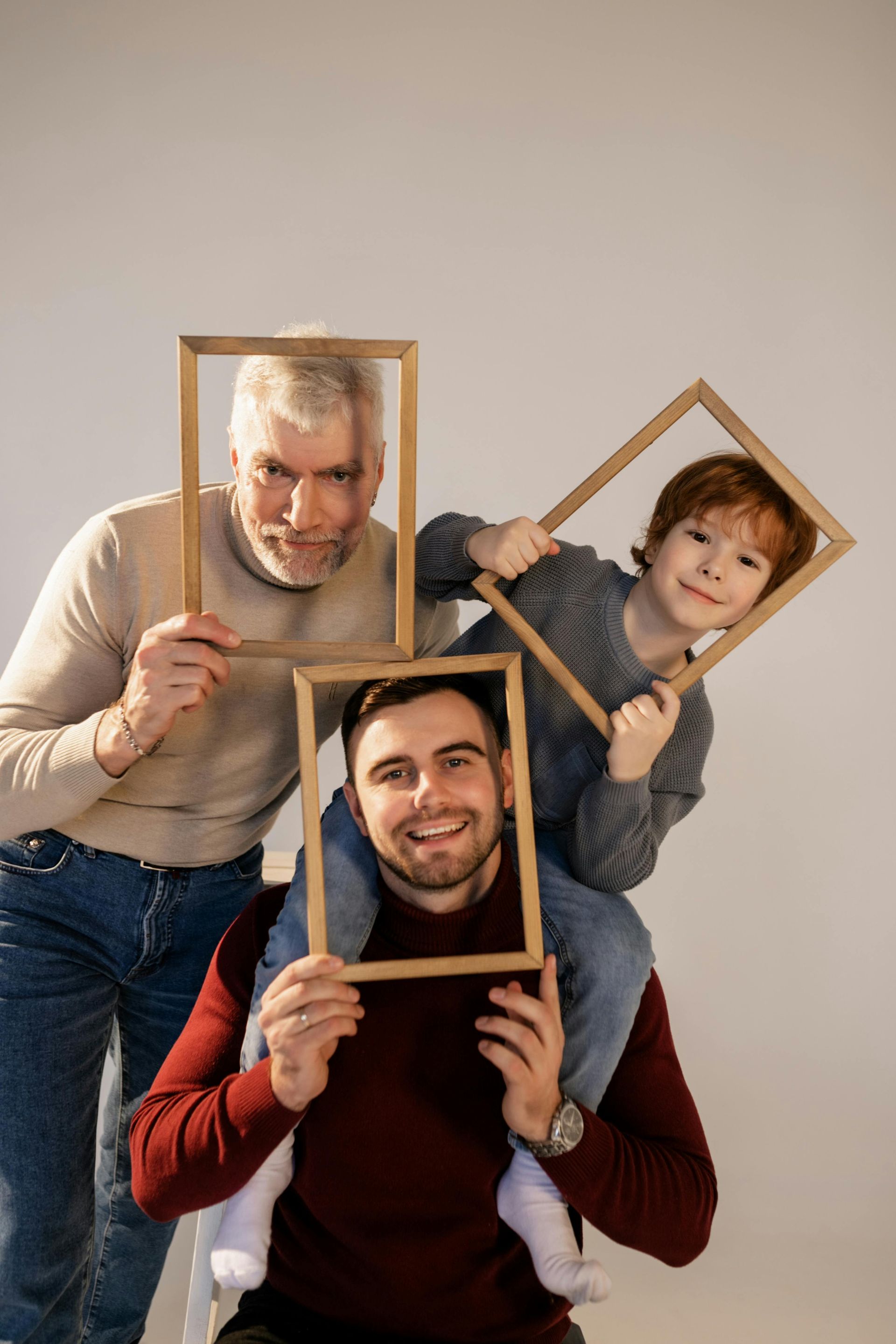 Three generations holding picture frames: grandfather, father, and son, smiling, posed indoors against a white backdrop.