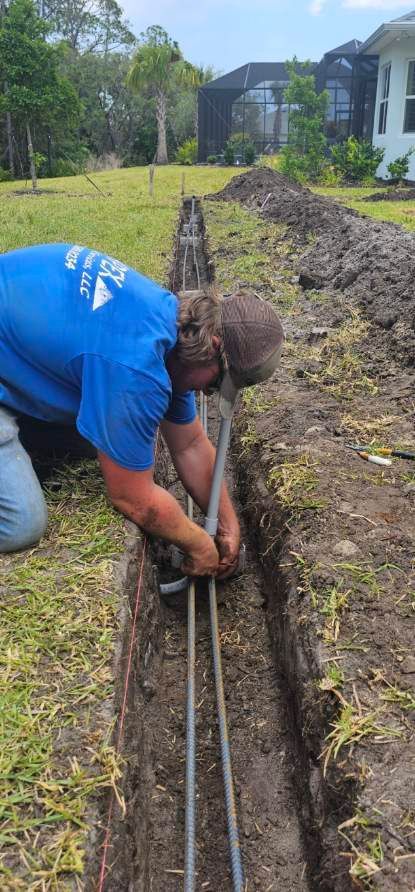 A man is kneeling down in the dirt working on a pipe.