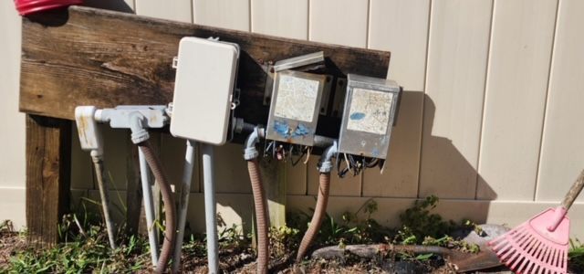 A bunch of electrical boxes are sitting on the ground next to a fence.