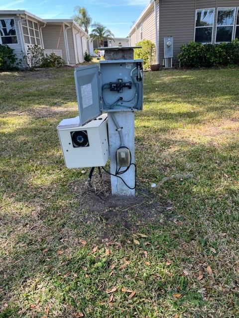 A white pole with a box on top of it in the grass in front of a house.
