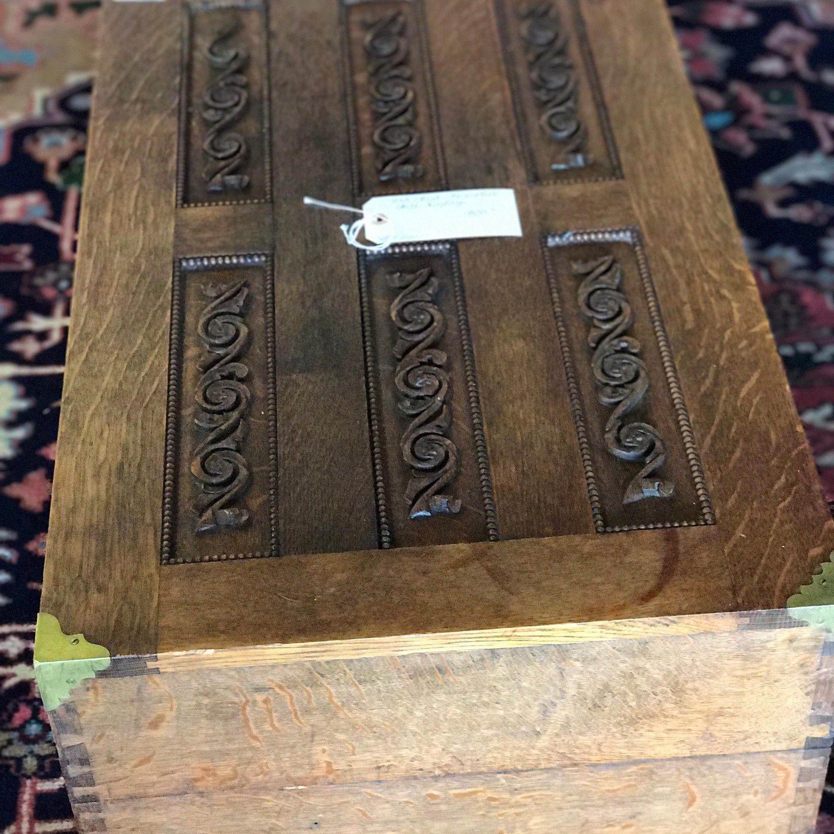 A wooden box with a tag on it is sitting on a rug.