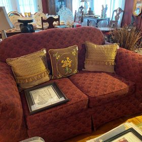 A red couch with gold pillows and a picture on it