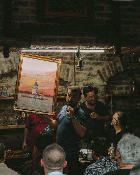 A man is holding a framed painting in front of a group of people.