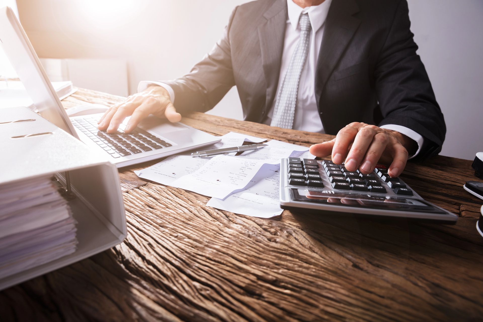 Un hombre con traje está escribiendo en una computadora portátil y usando una calculadora.