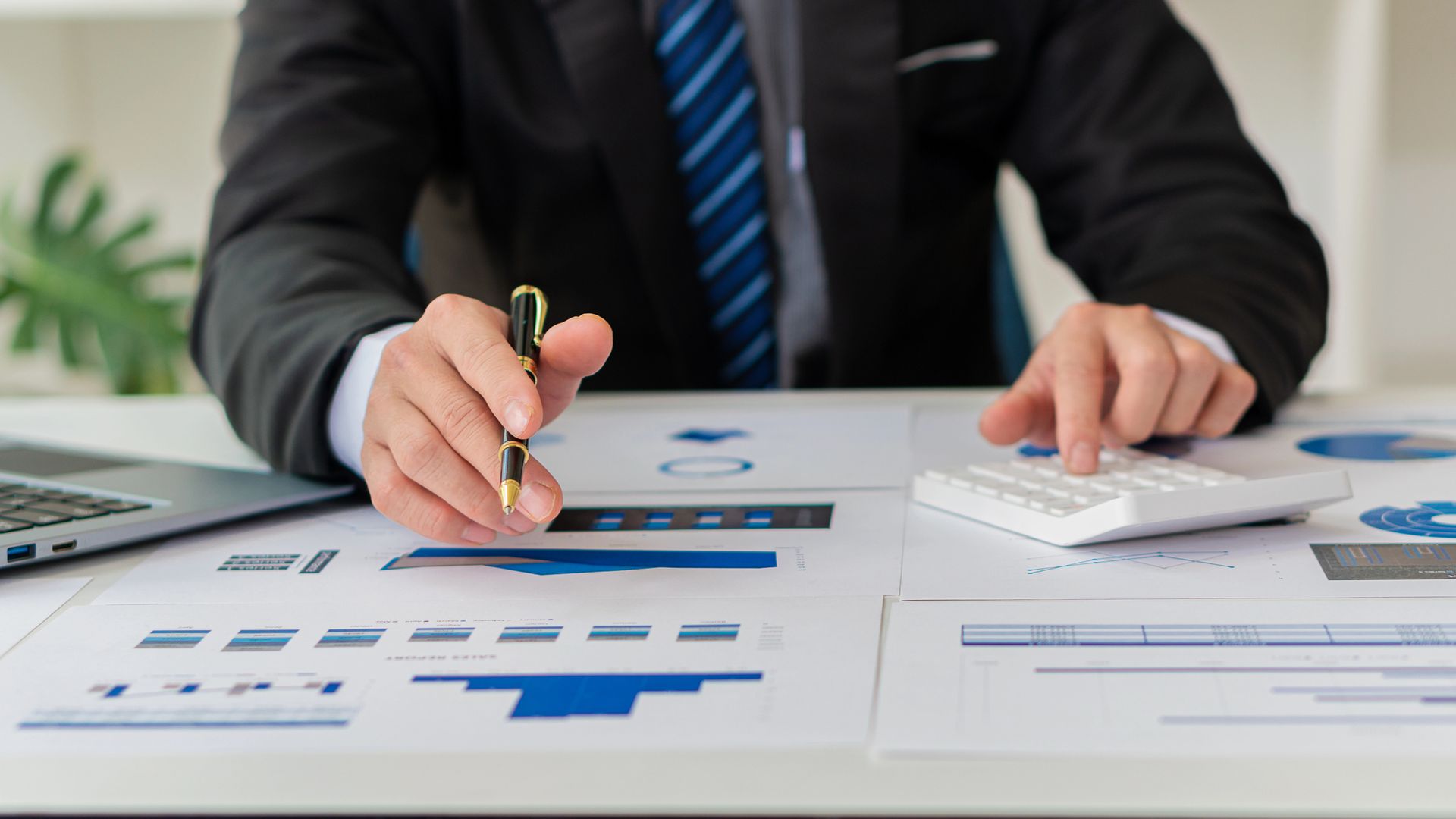 Un hombre con traje y corbata está sentado en un escritorio usando una calculadora.