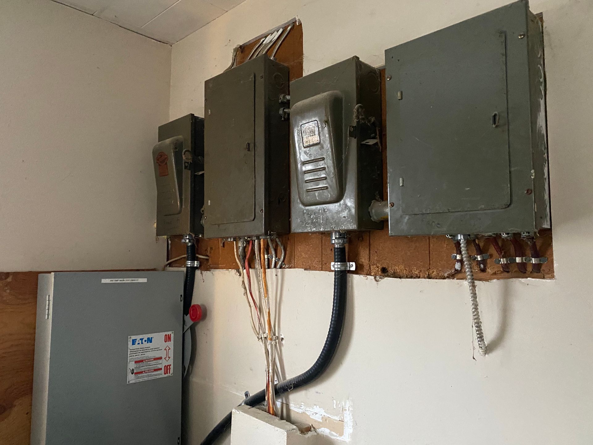 Electrical panel and boxes on a wall. Wires and conduit connect the metal boxes. A power box is on the left.