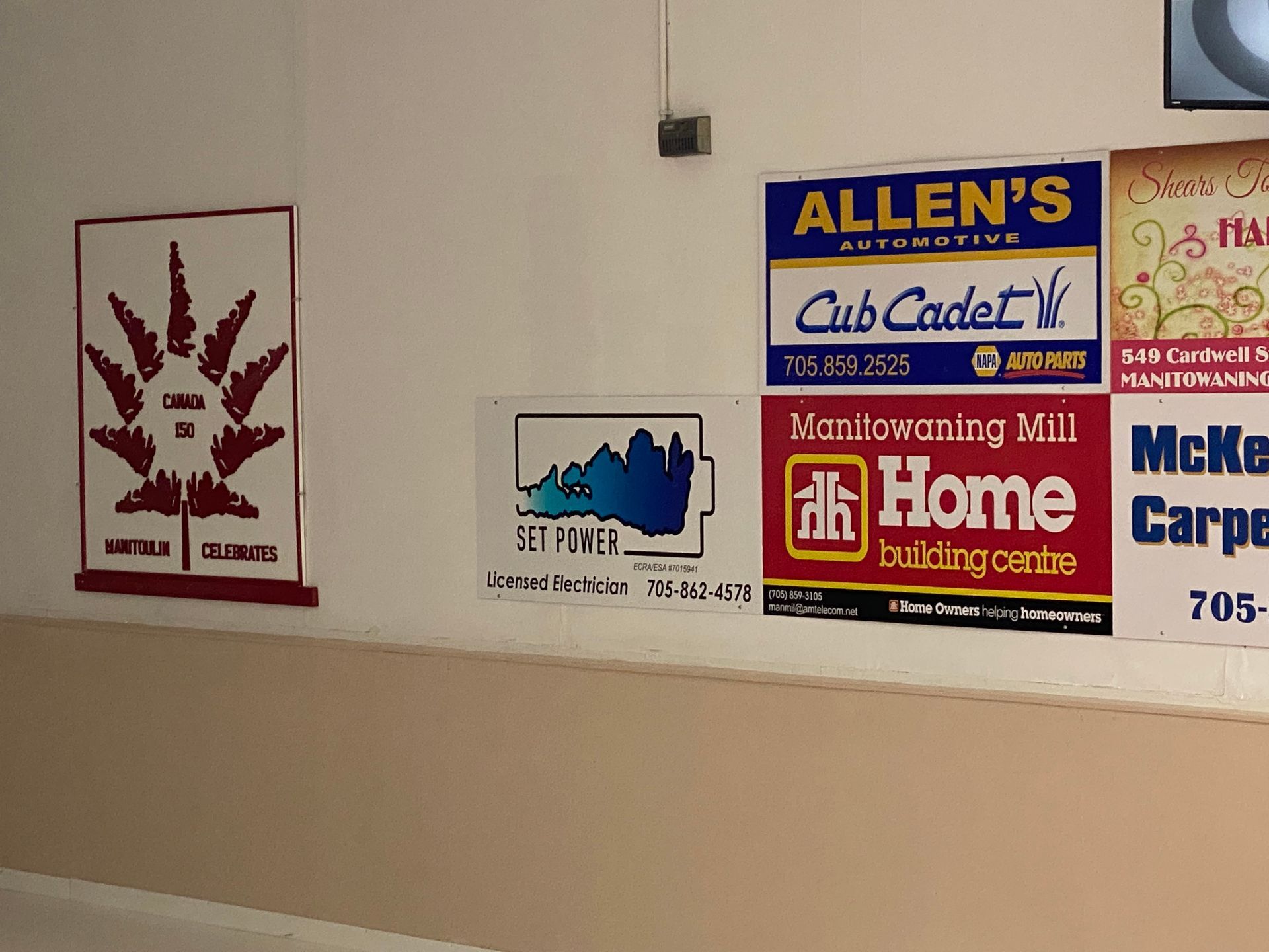 Wall with signs: Allen's Automotive, Manitouwaning Mill, Home building centre, and other businesses.