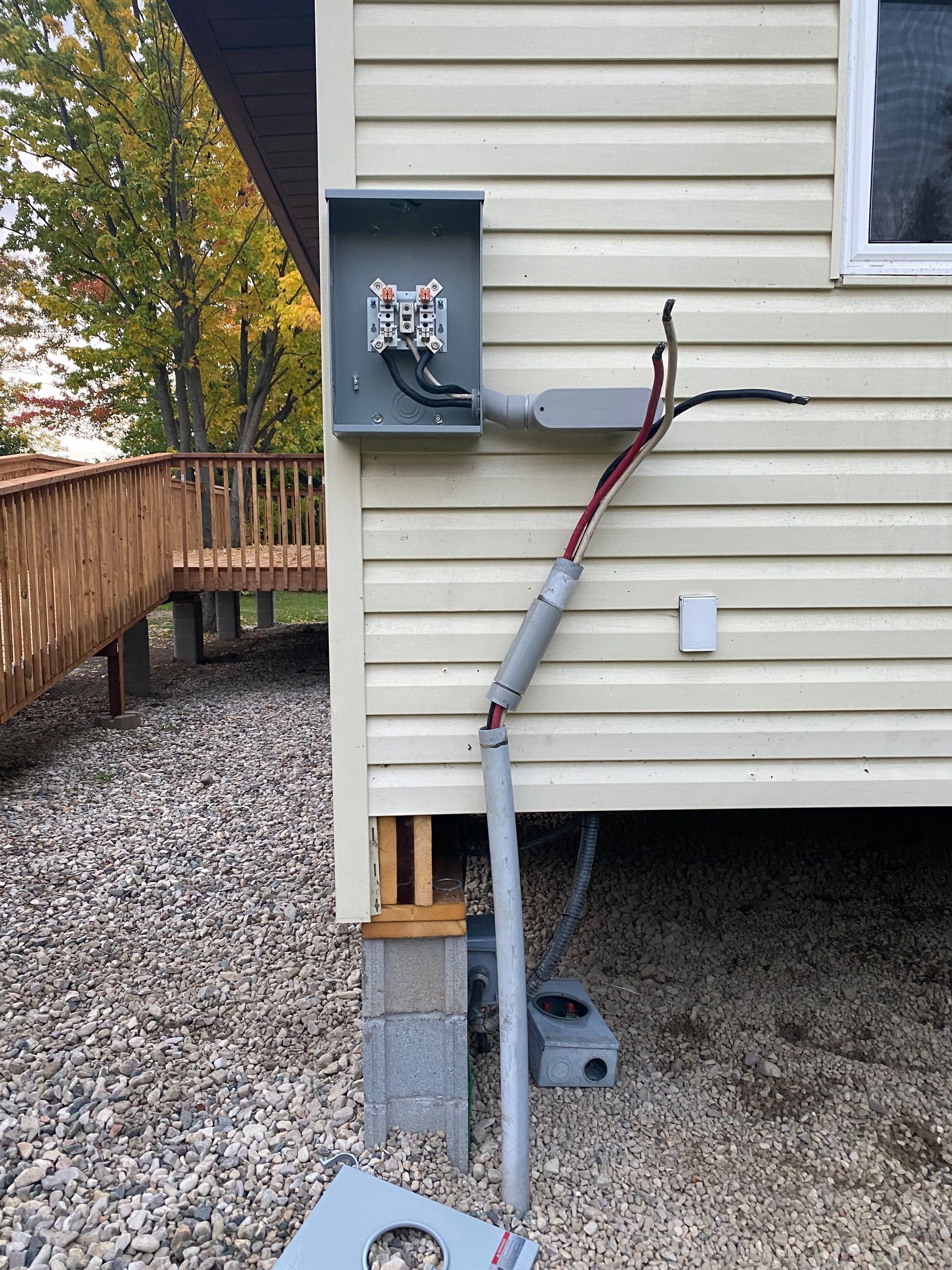 Electrical service equipment on a house exterior. Gray conduit and wiring visible against light-colored siding.
