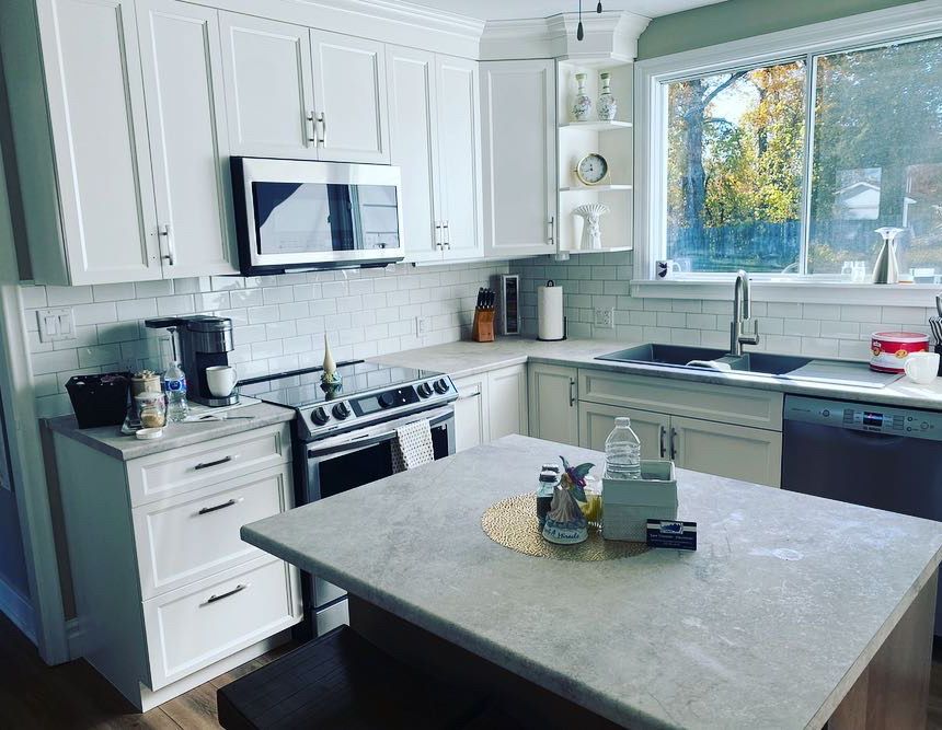 White kitchen with light countertops, built-in appliances, and a central island near a window.