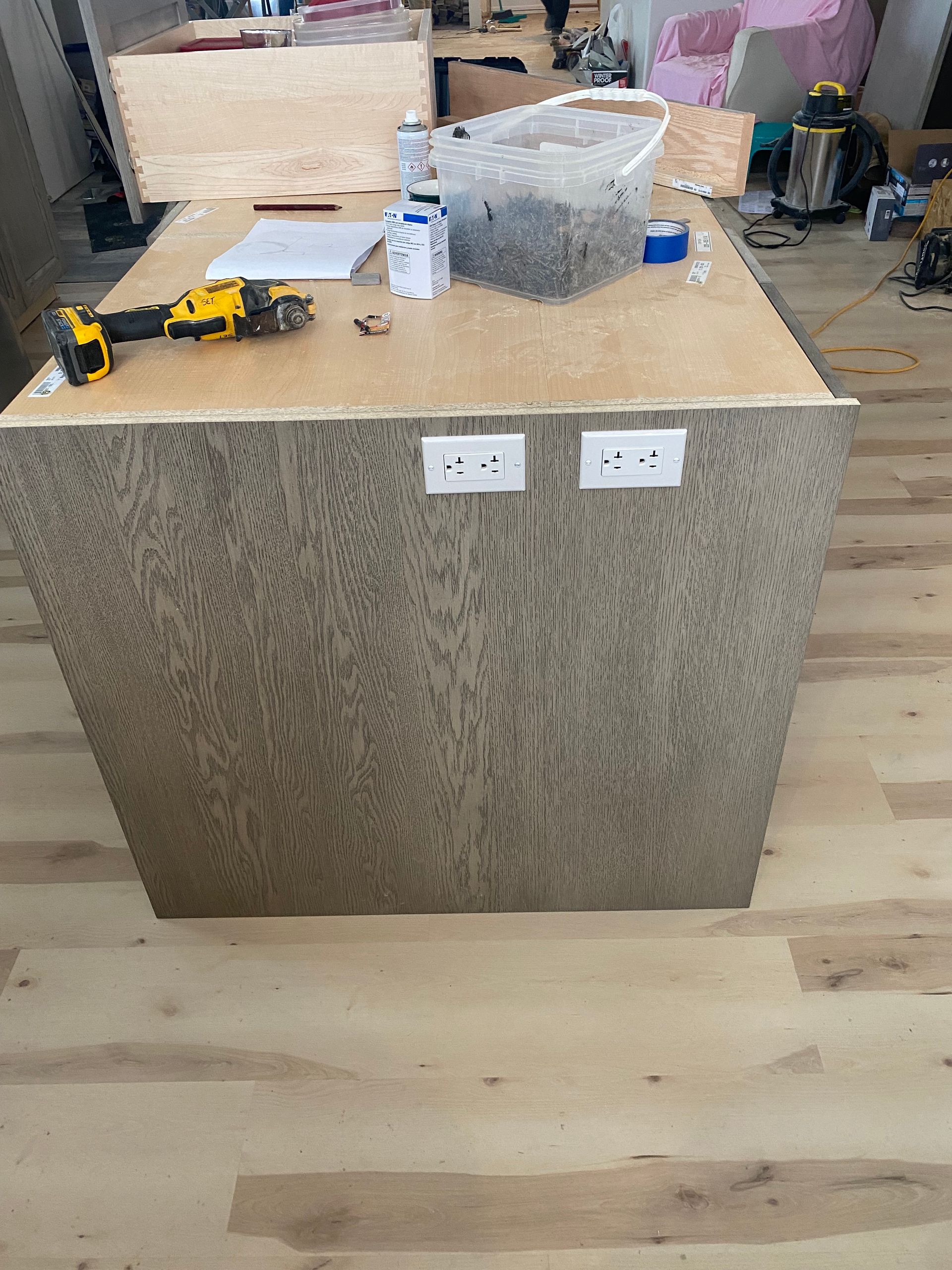 Kitchen island with wood-grain panels, two electrical outlets, and tools and materials on the countertop.