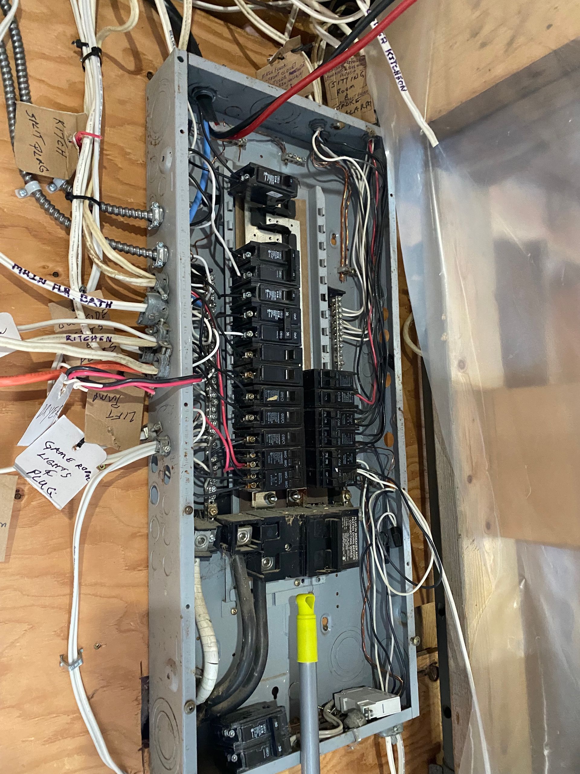 Electrical panel with numerous wires attached, mounted on wood paneling.