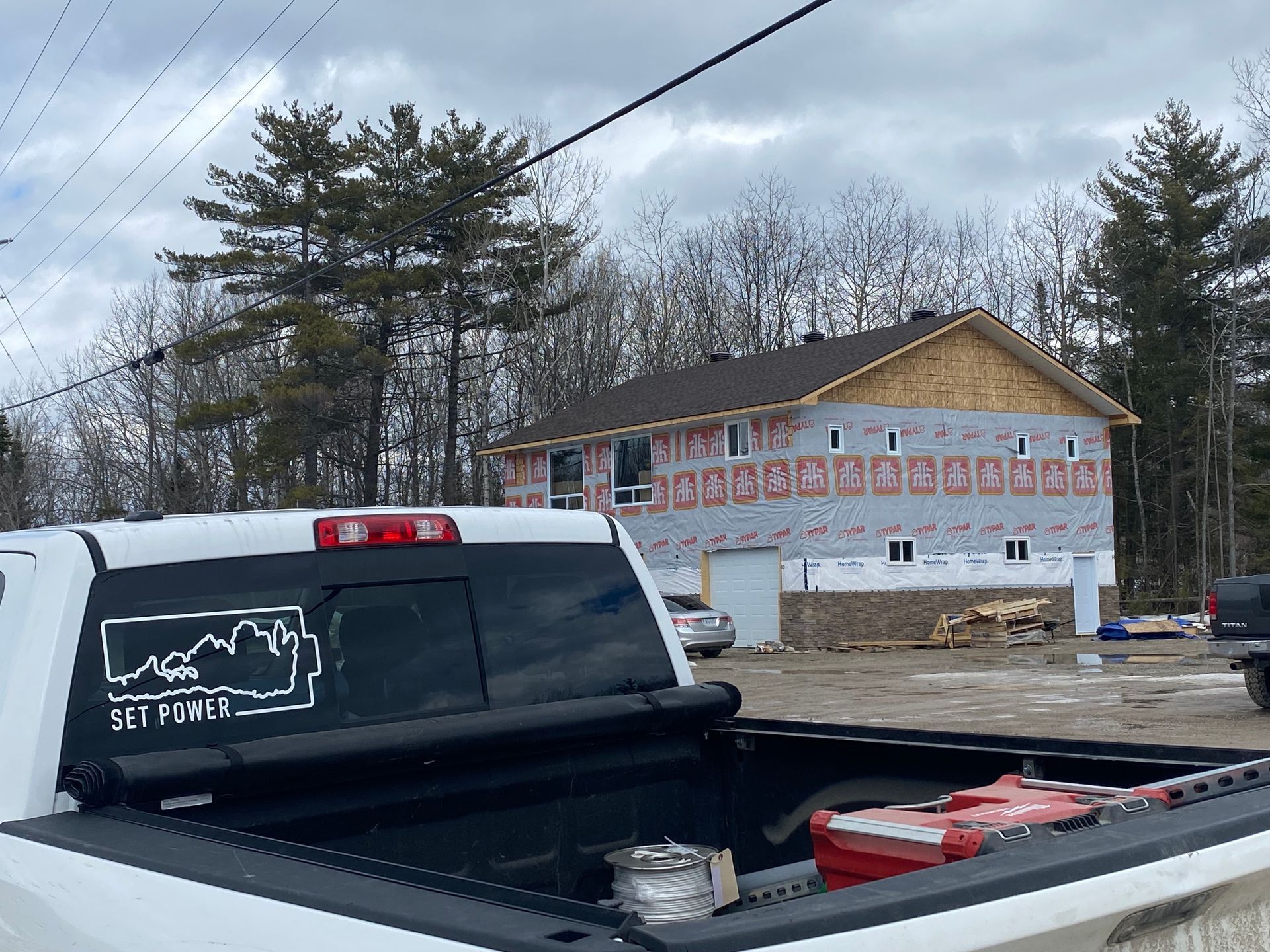 White pickup truck in front of a house under construction. Trees in the background. Cloudy sky.