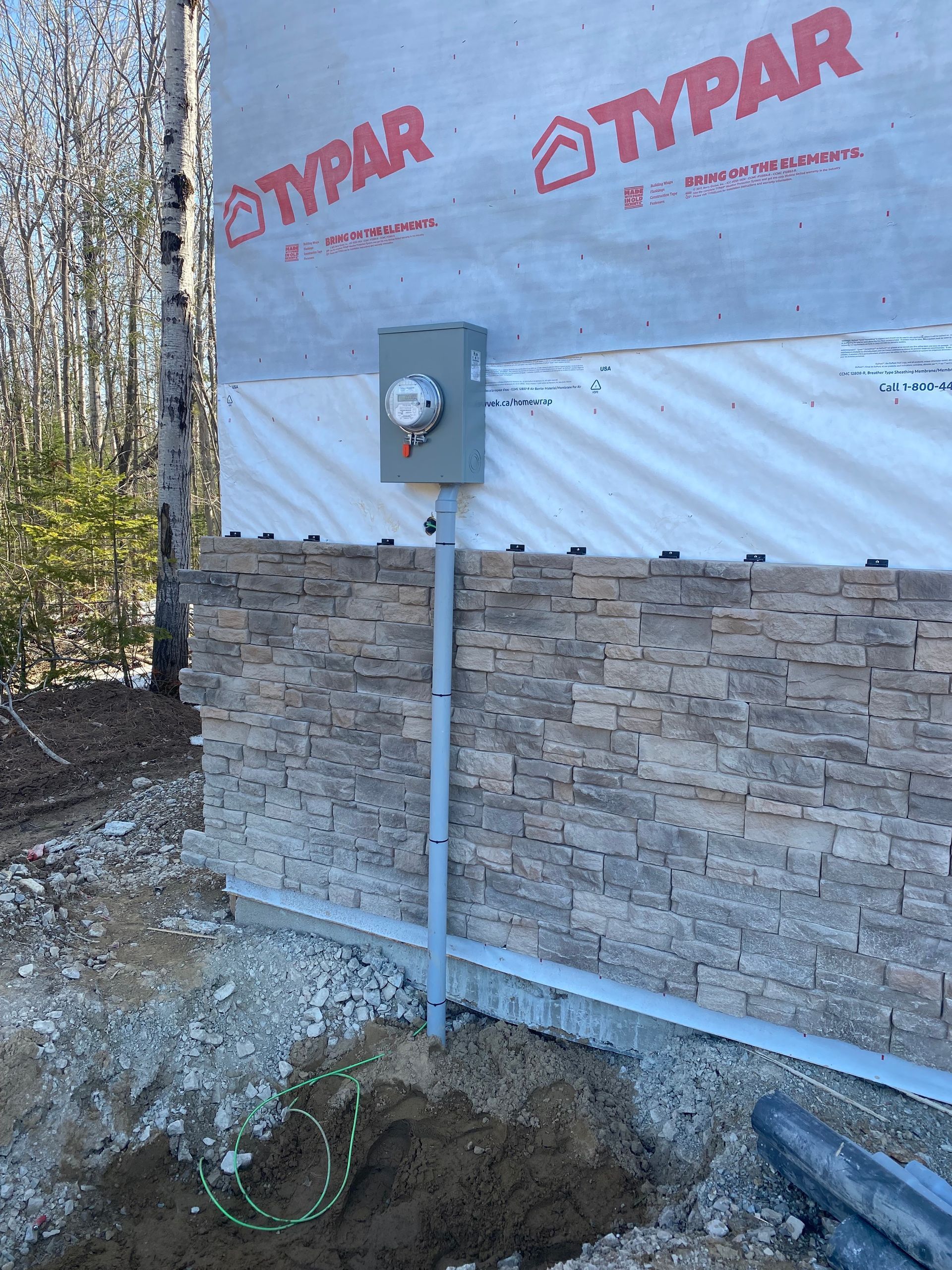 Electrical meter box on a building's stone facade, with conduit and grounding wire visible.