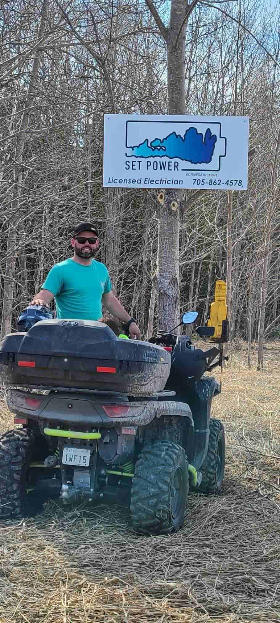 A man on an ATV in a wooded area, with a sign that says 