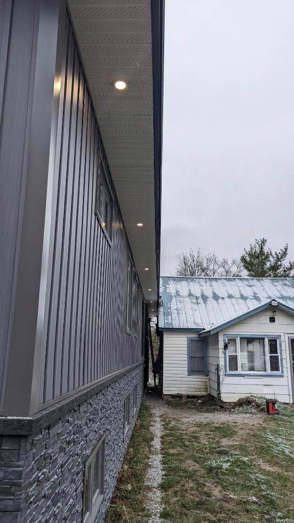 Side view of two buildings: modern building with stone and siding next to a small white house, snow on the ground.
