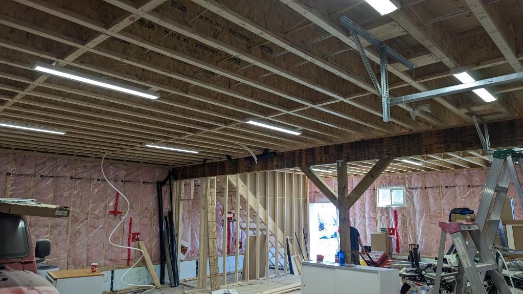 Interior view of a building under construction, with exposed wooden beams, insulation, and workers visible.