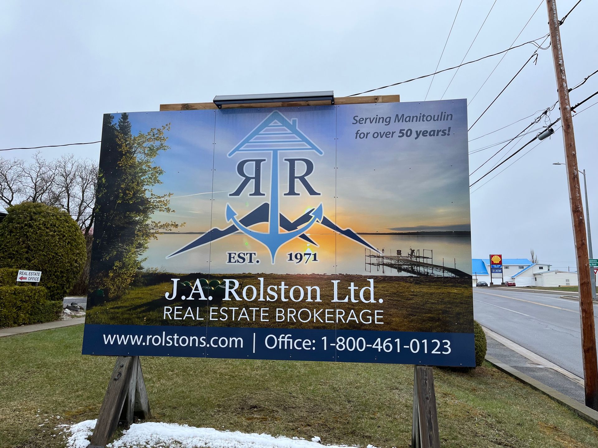 Real estate sign for J.A. Rolston Ltd., showing logo with mountains, an anchor, and a lake scene.