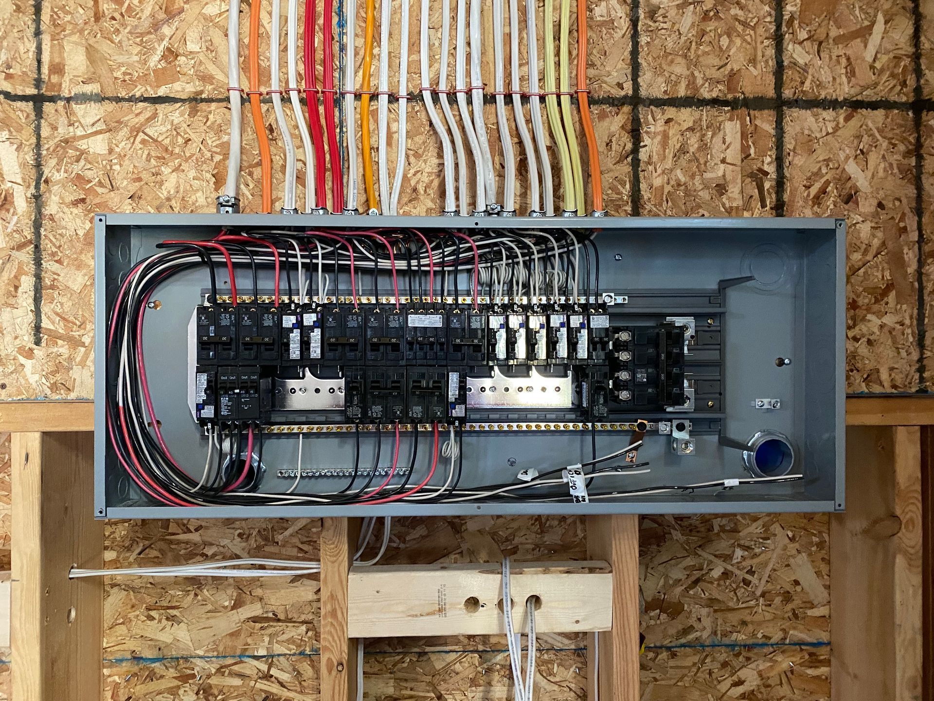 Electrical panel with wires and circuit breakers mounted on a wood wall.