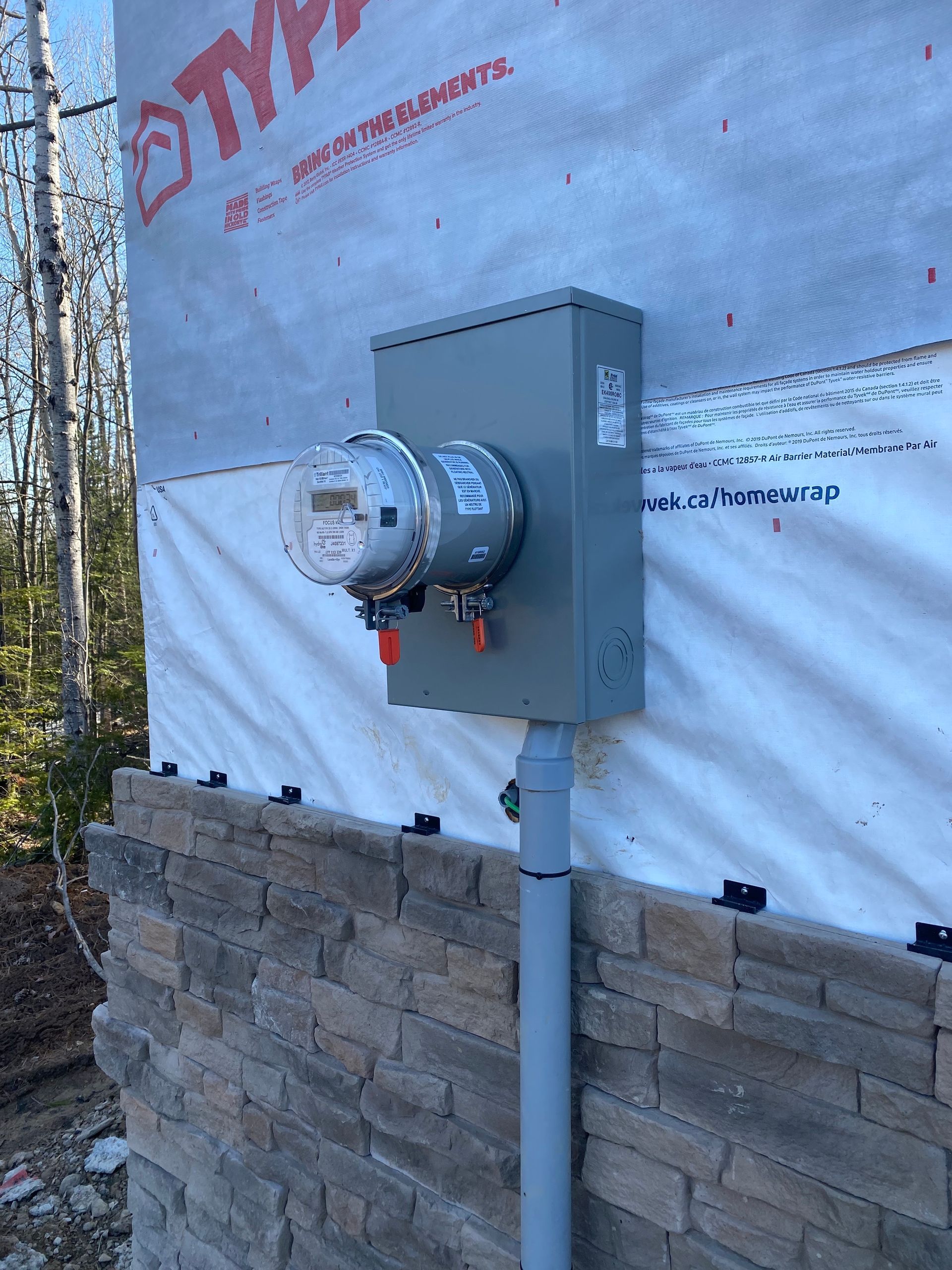 Electric meter and panel mounted on a house exterior, gray and tan color scheme.
