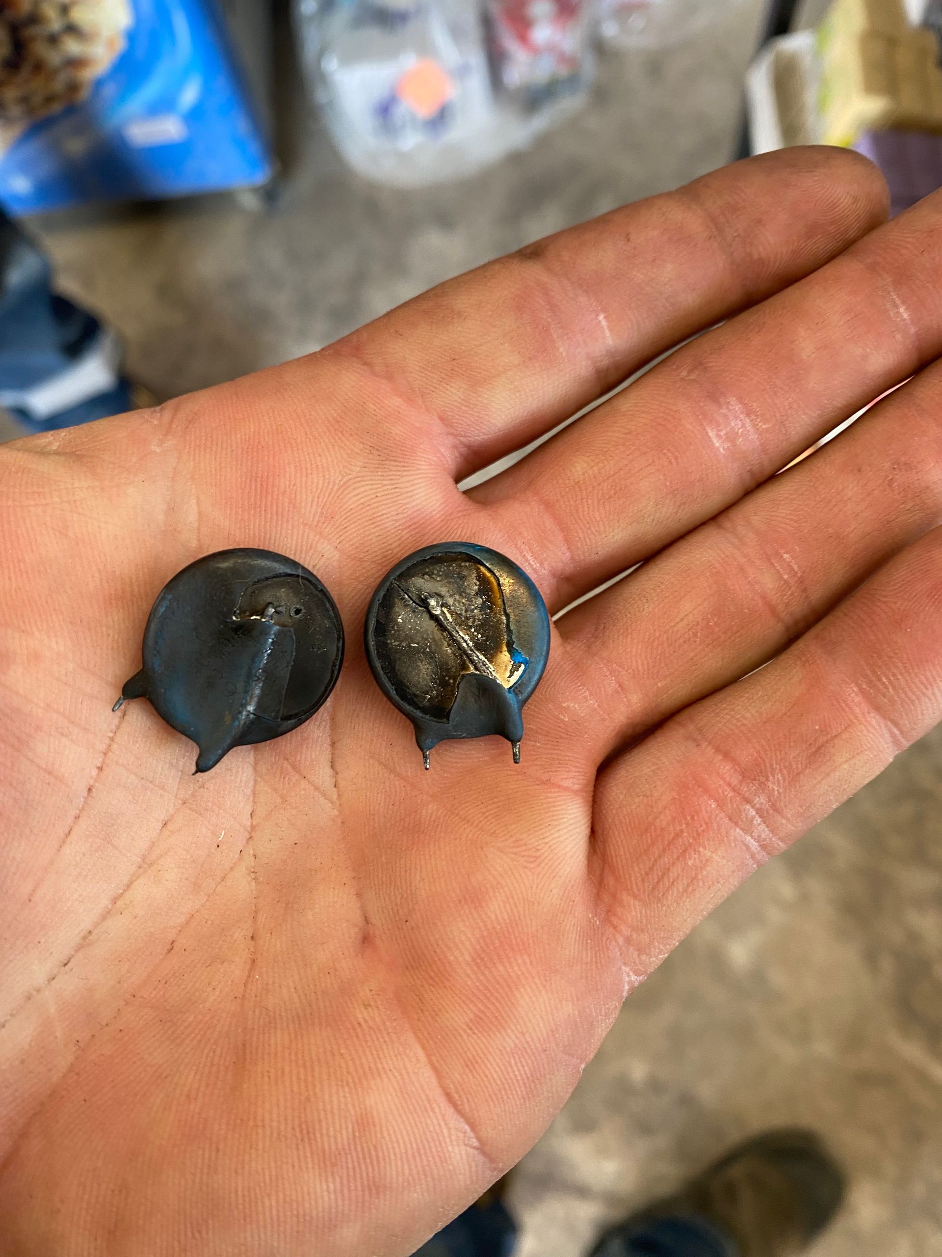 Two small, round, dark blue metal objects with protruding legs, held in a person's hand.