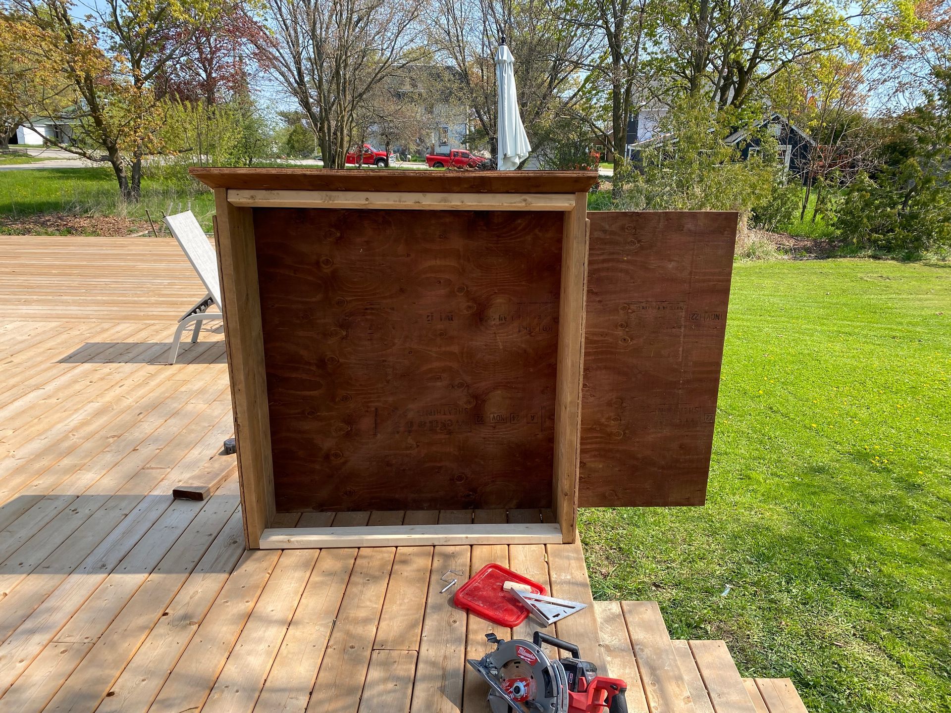 Wooden outdoor storage box with open door on a wooden deck.