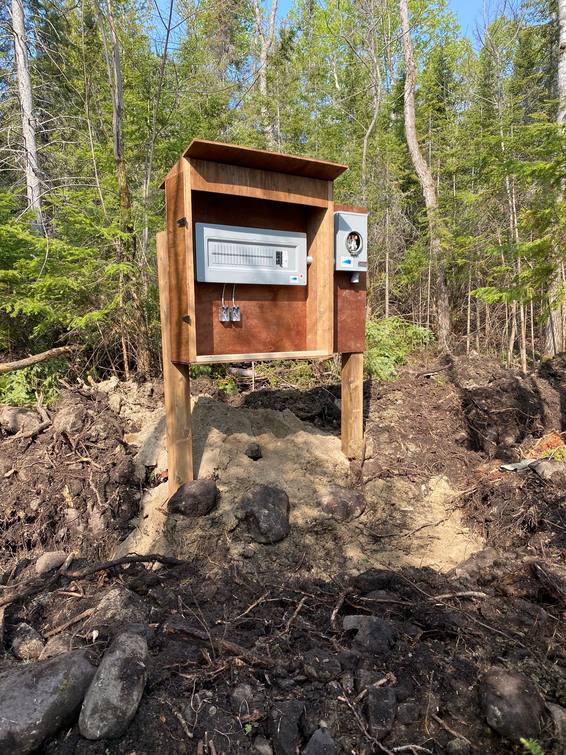 Wooden electrical box on posts in a wooded area. The ground around the box is dirt.