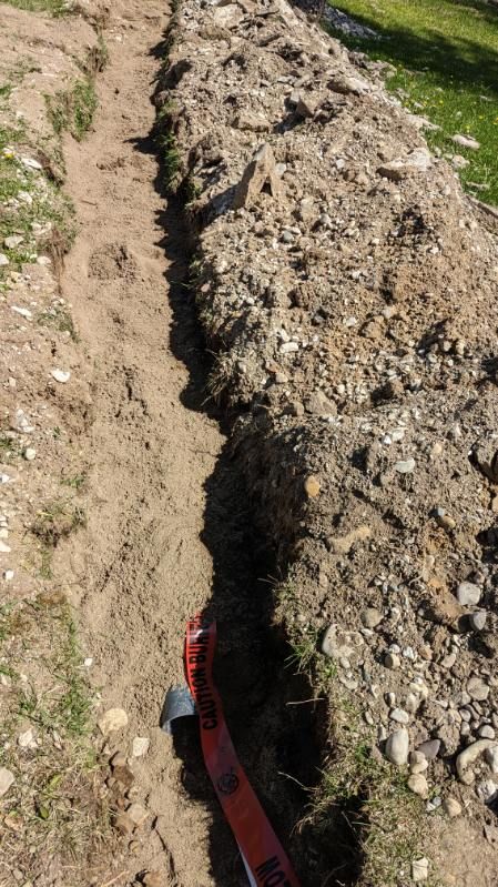 A trench dug in the ground, with dirt pile alongside. A utility cable is visible.