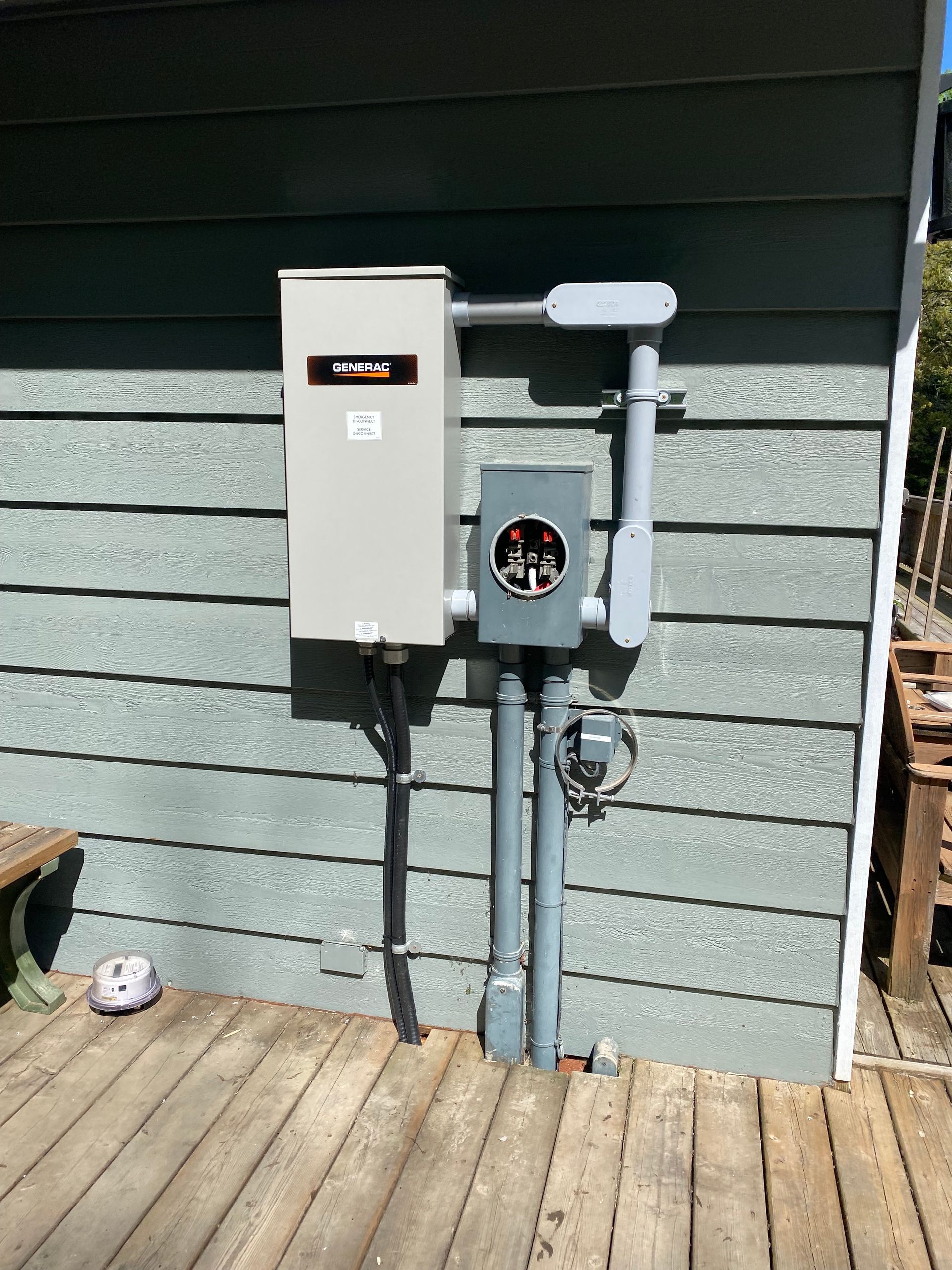 Electrical panel and meter box mounted on a house exterior with gray siding.