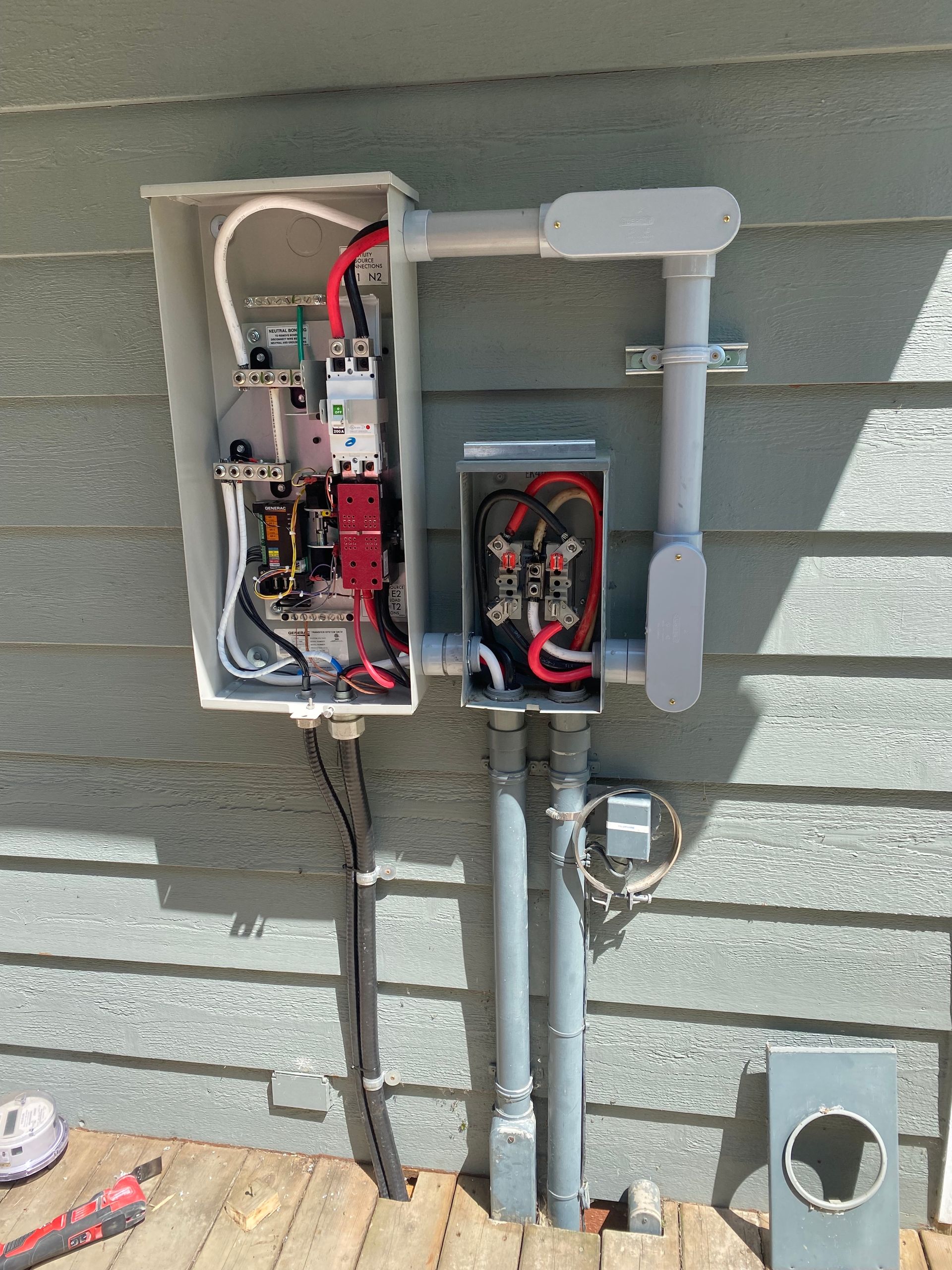 Exterior electrical panel with conduits and wiring on a siding wall.
