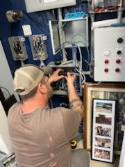 Man in cap working on electrical wiring in a utility room.