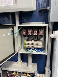 Open electrical box with four relays, wiring, and conduit on a blue wall.