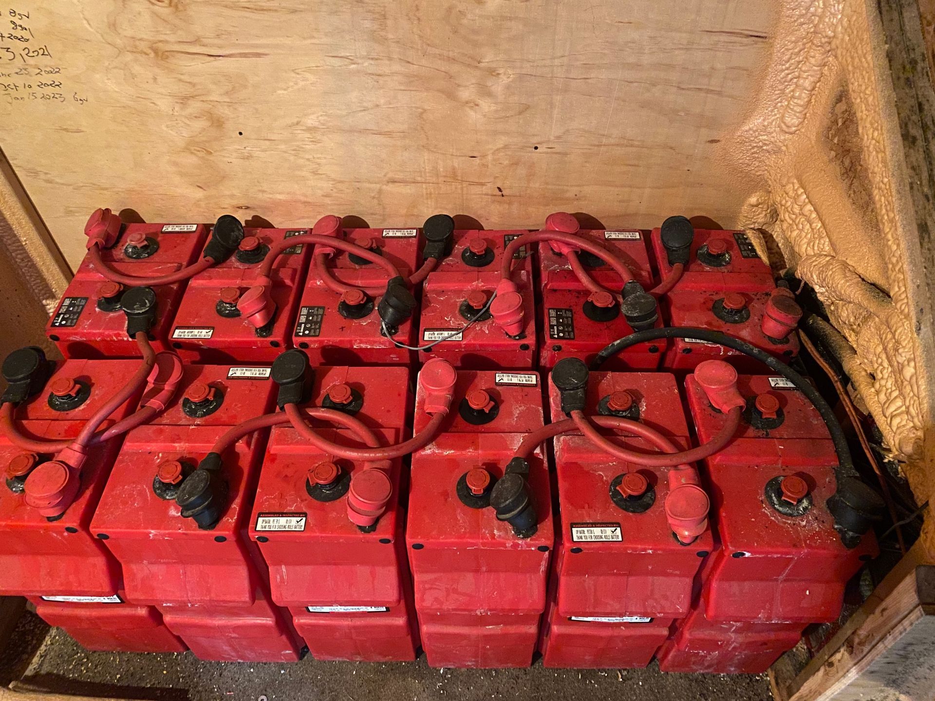 Red batteries connected by red cables, arranged in a wooden enclosure.