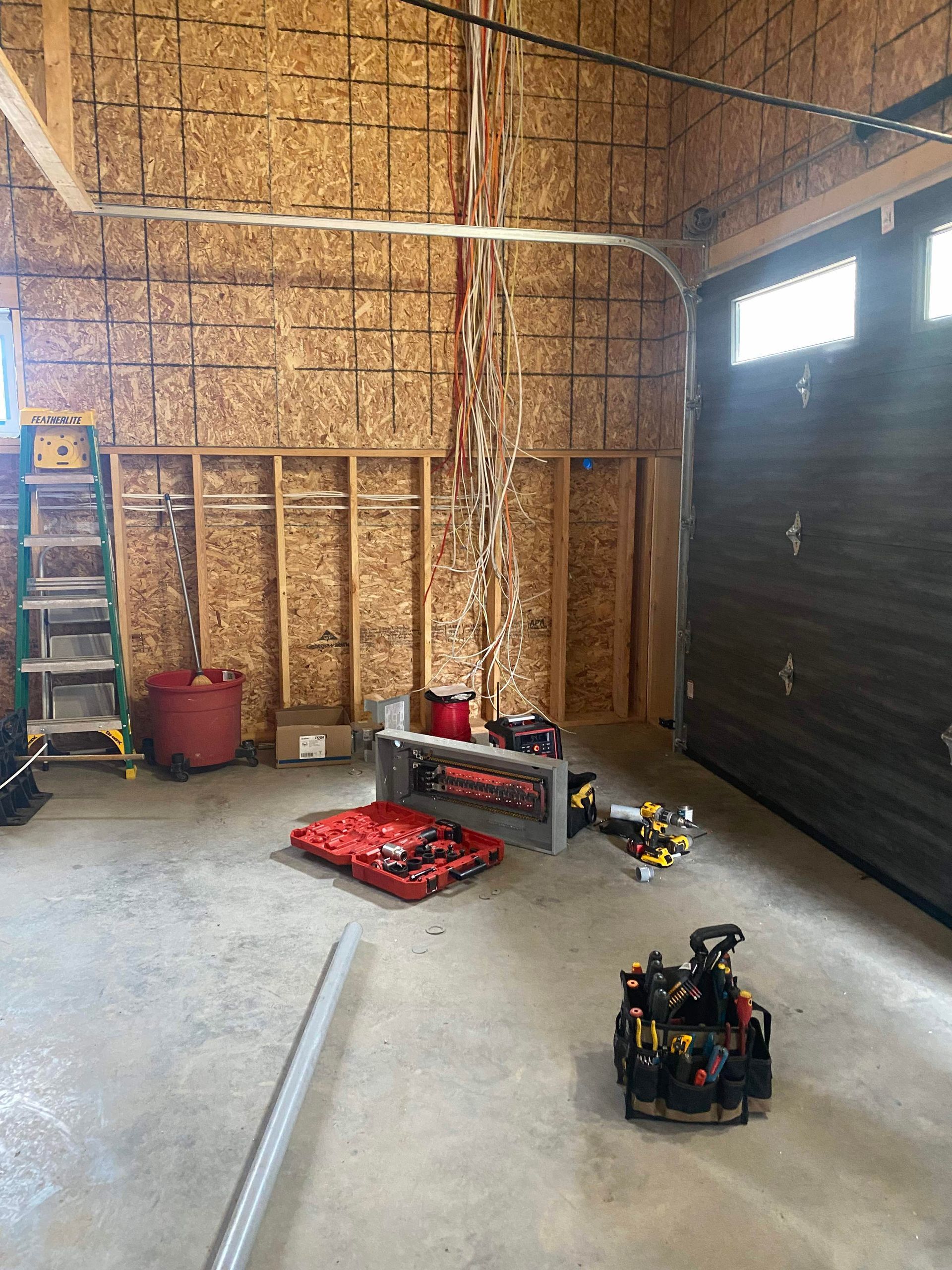 Garage interior under construction; electrical wiring, tools, and a garage door.
