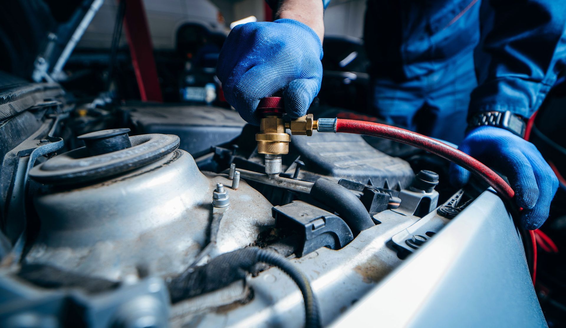 Mechanic working on a car engine, connecting a hose. Wearing blue gloves.