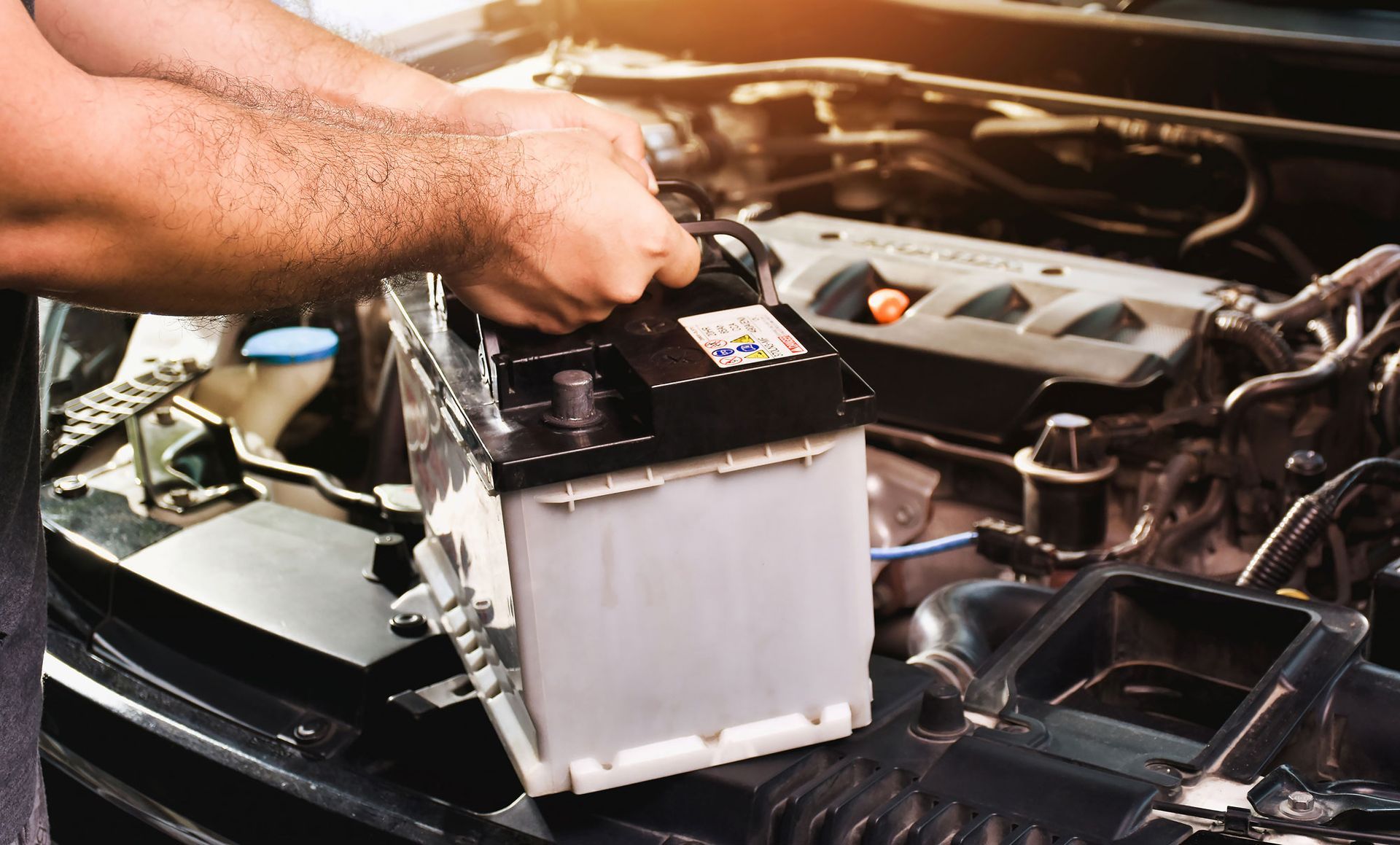 Person replacing a car battery in an engine bay.