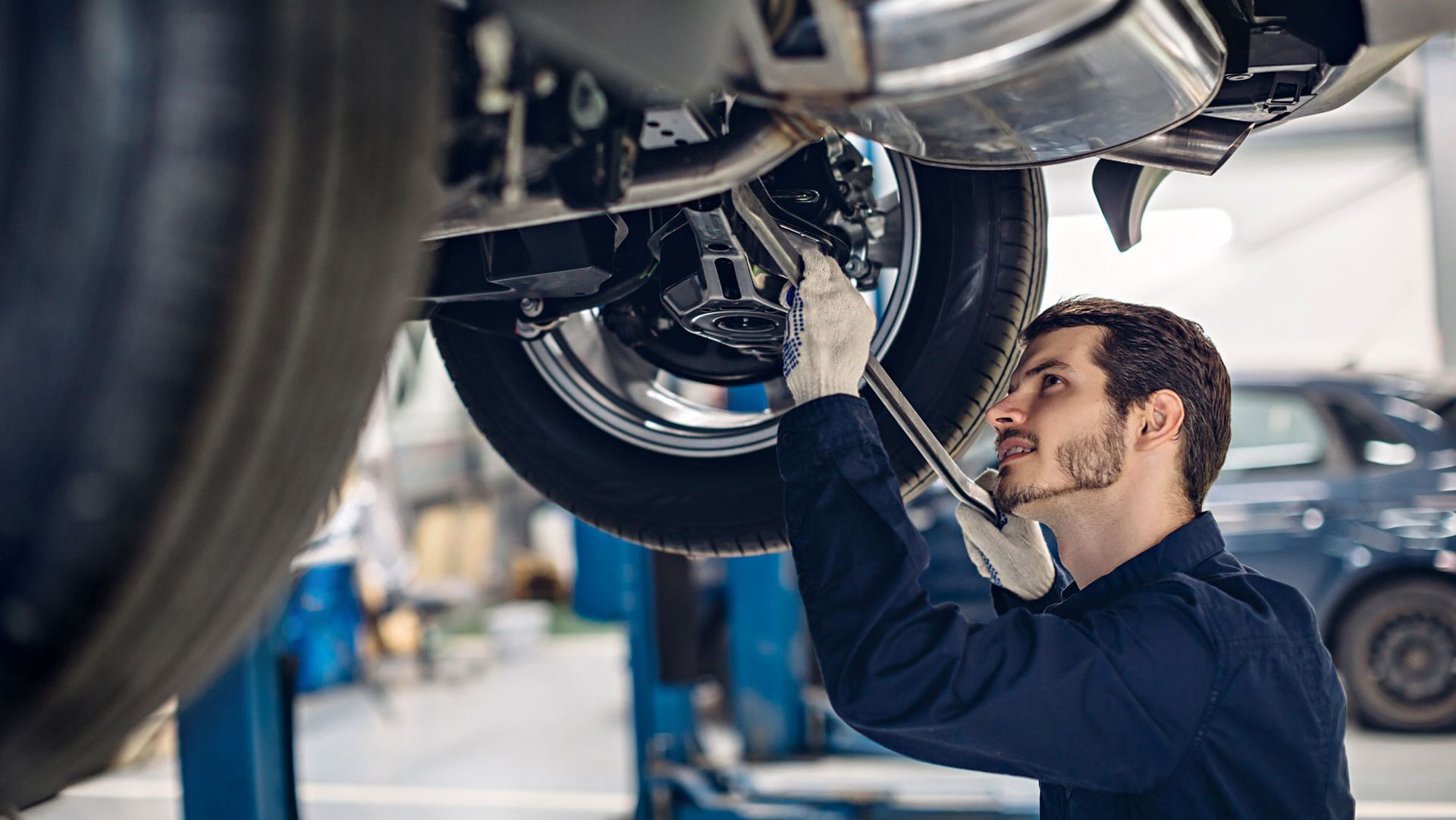 Mechanic under a car, working on brakes, in a shop.