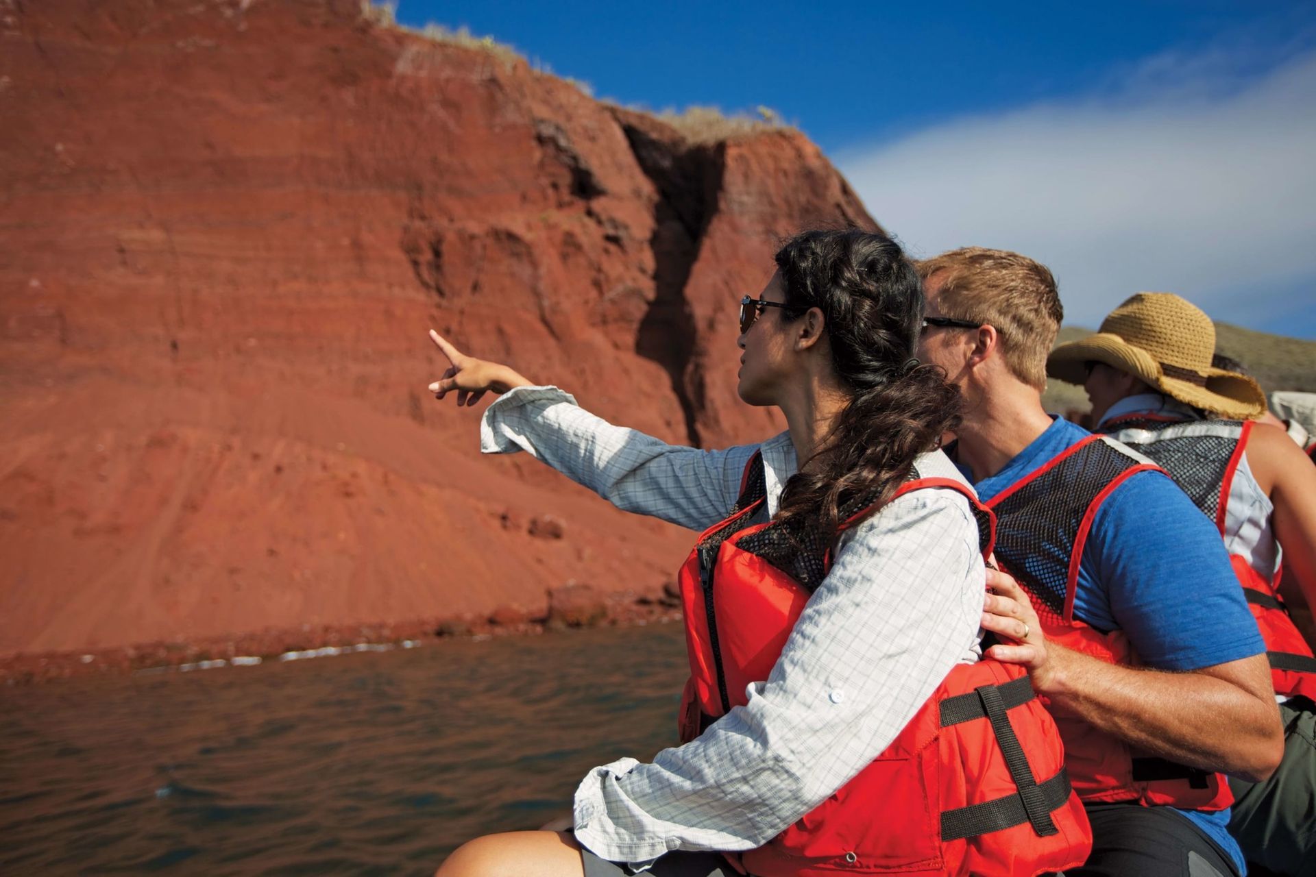 A woman in a life jacket is pointing at something while sitting on a boat.
