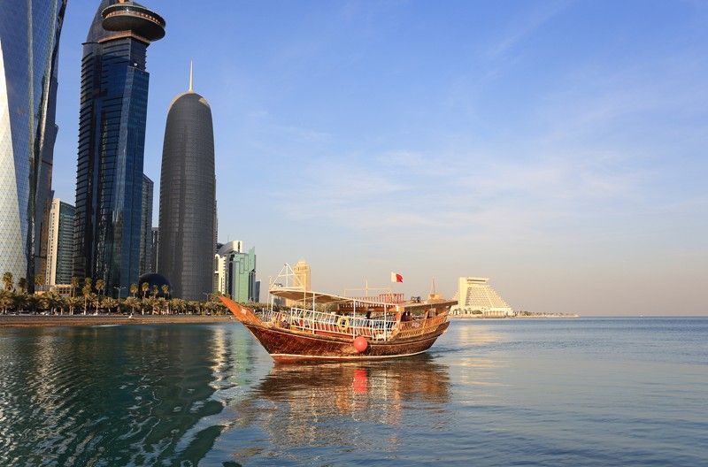 A boat is floating on top of a body of water in front of a city skyline.
