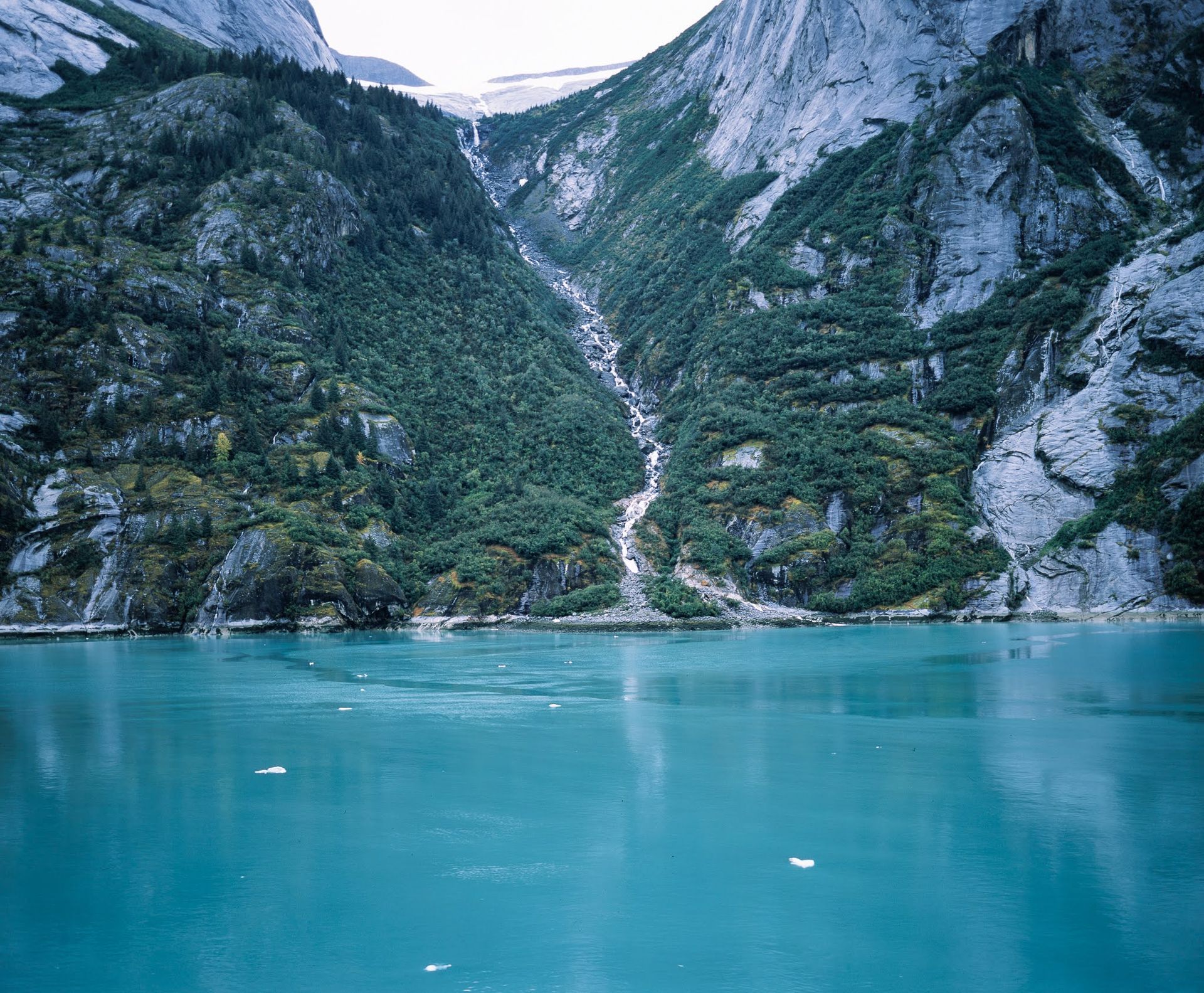 Turquoise lake below steep rocky mountains with a narrow waterfall