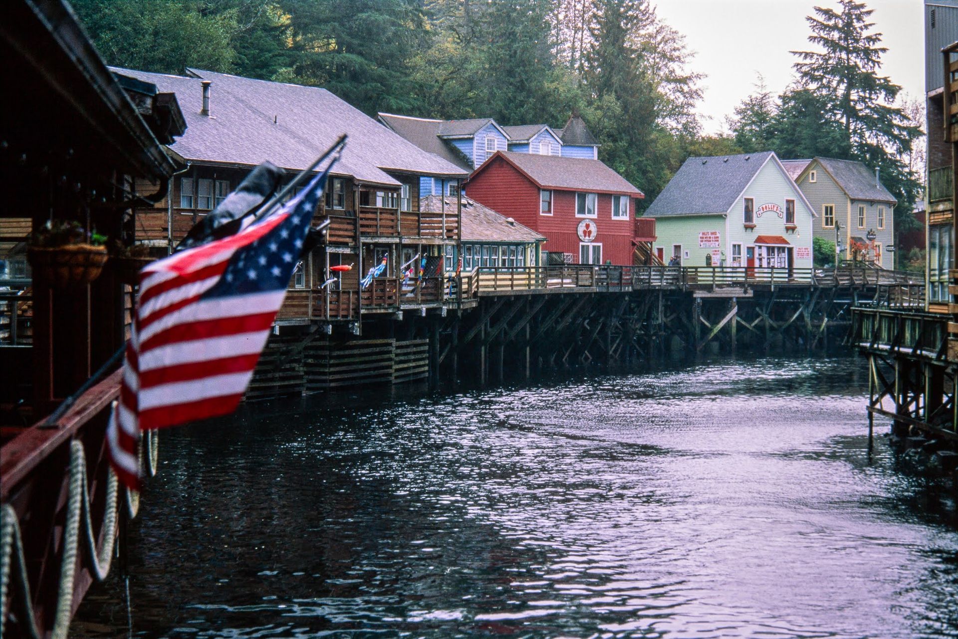 American flag on a wooden waterfront dock beside colorful buildings over calm water