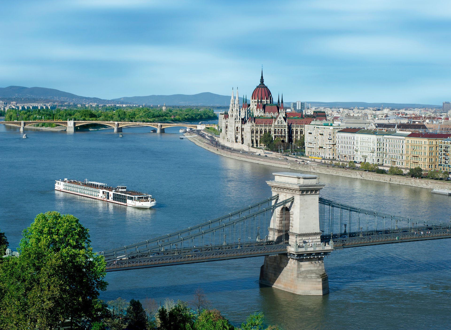 Budapest cityscape: Danube River with a cruise ship, Parliament building, and Chain Bridge. Blue sky and water.