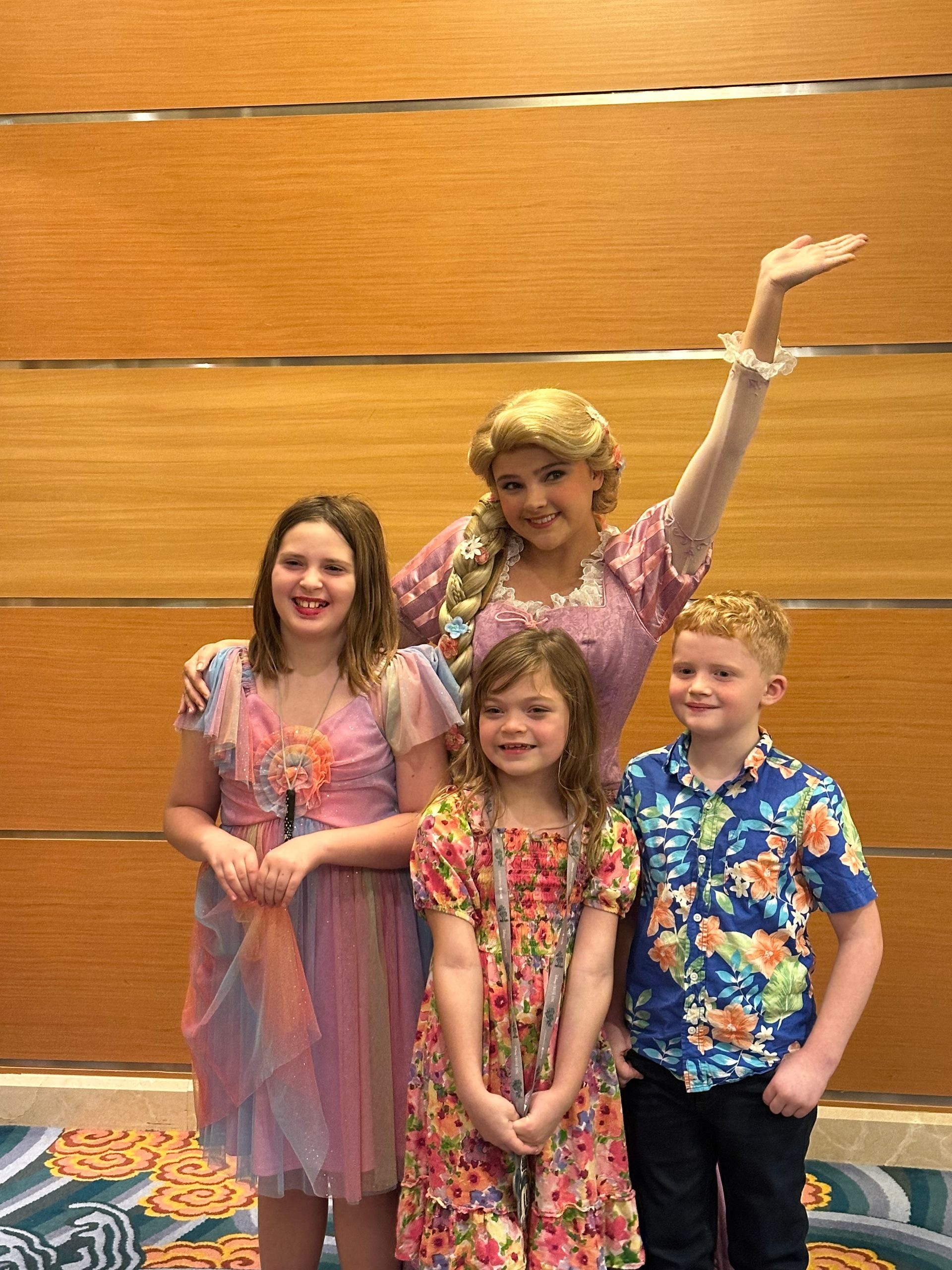 Four children pose with a woman dressed as Rapunzel against a wood-paneled wall.
